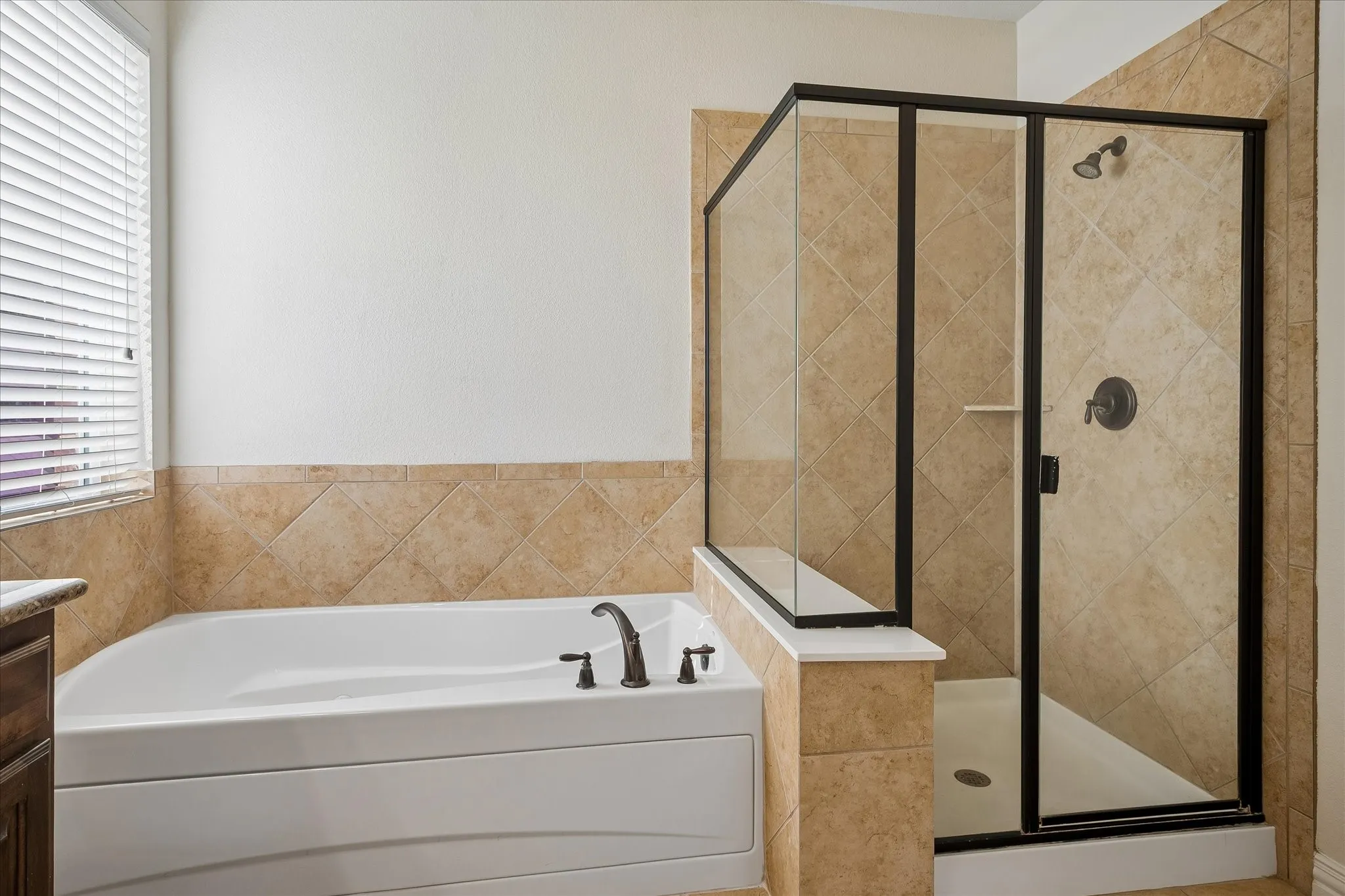 Built-in soaking tub with bronze-finish fixtures, tile surround, and an enclosed shower with a glass and bronze-finish frame