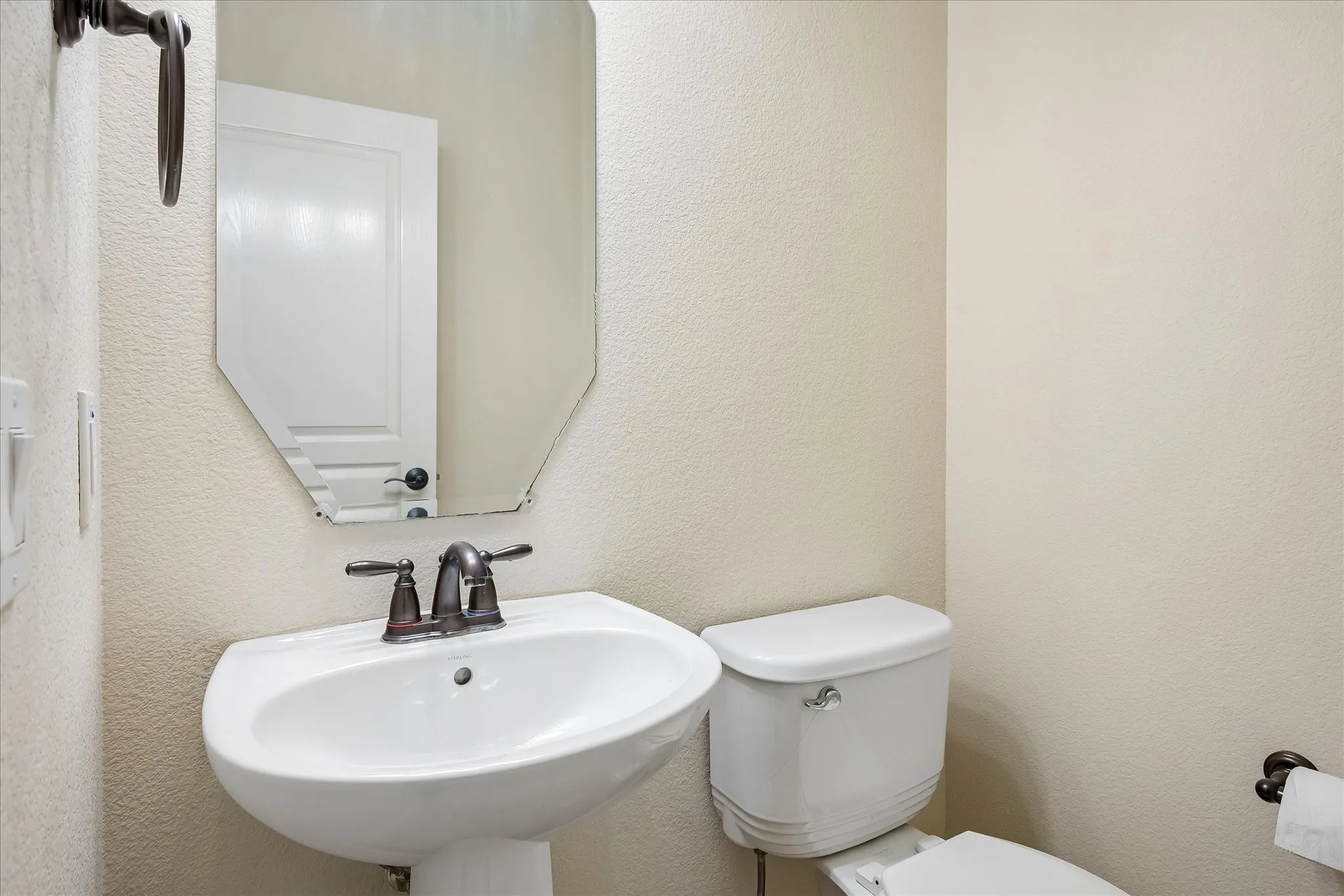 Pedestal sink with bronze-finish faucet, octagonal wall mirror, and white toilet