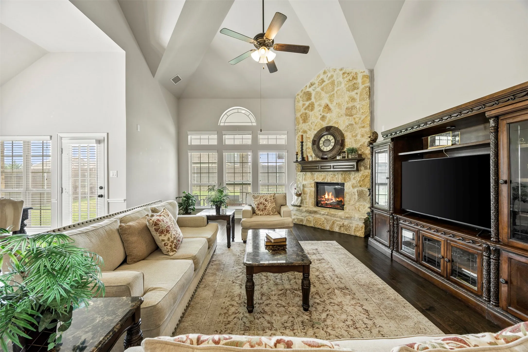 Great Room with vaulted ceilings, a stone-faced fireplace, dark wood-finish flooring, and all the windows you need for abundant natural light