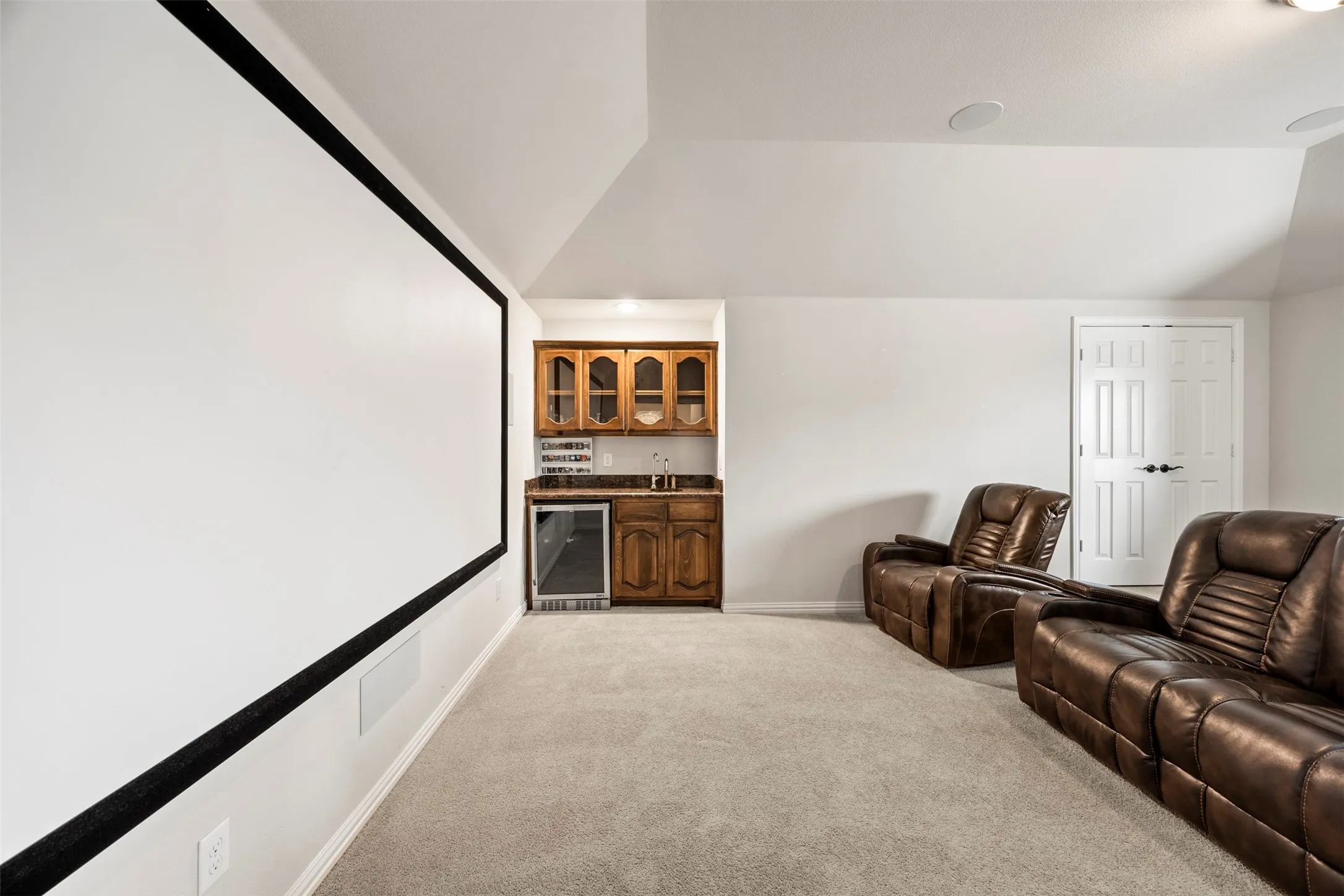 Dedicated entertainment space with a large projection screen, built-in wet bar, and recessed speakers