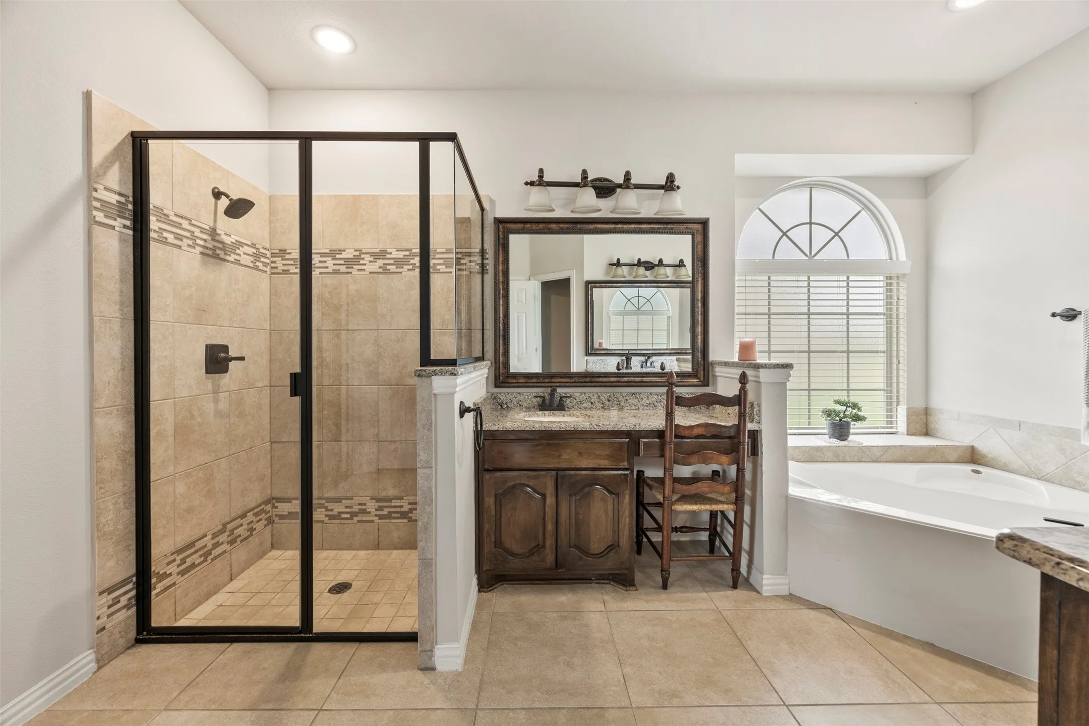 Full bathroom featuring a walk-in shower with a glass enclosure, a built-in soaking tub, a vanity with a stone countertop, a framed mirror, and tile flooring