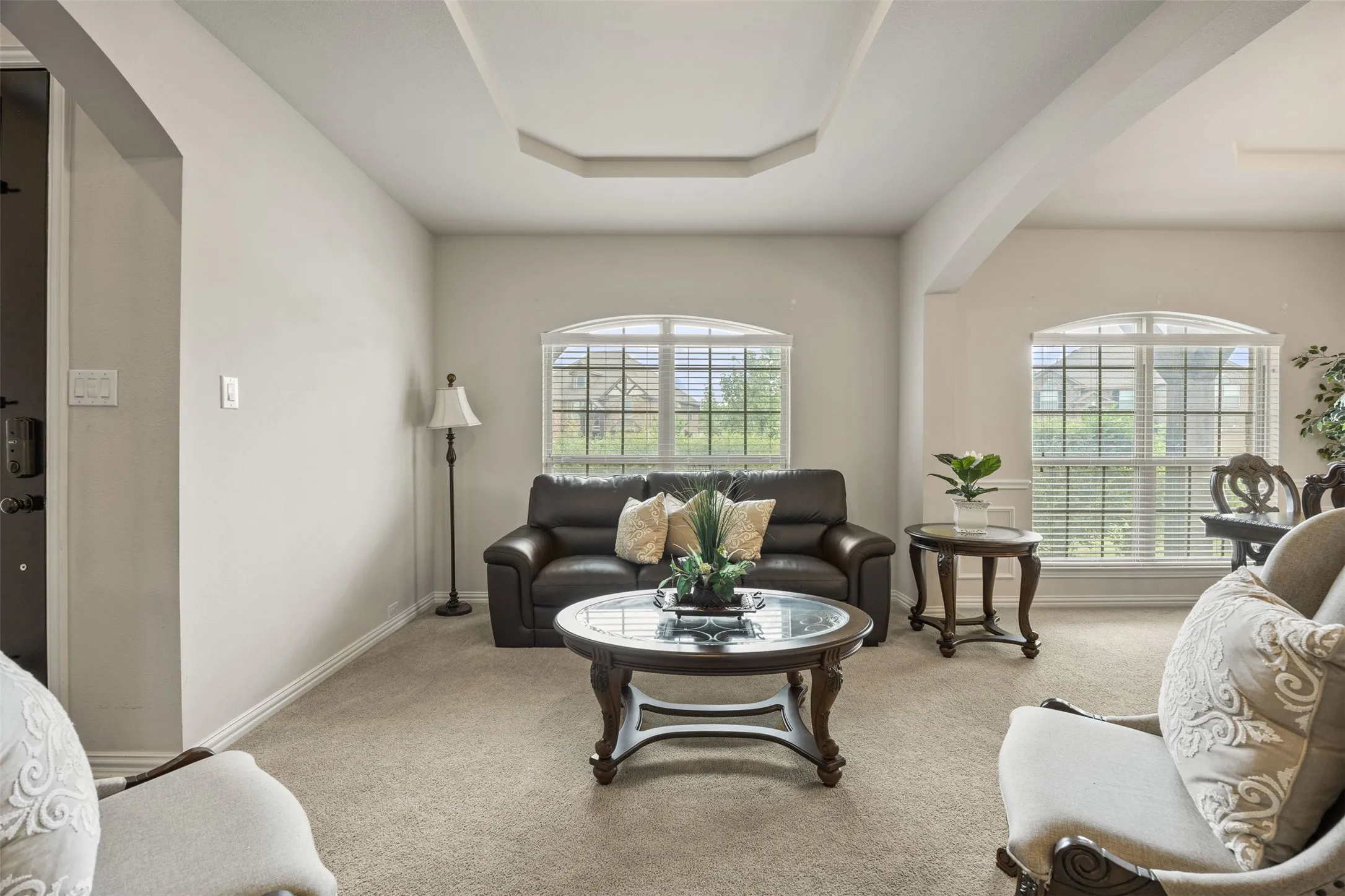 Living Room with dual arched windows, a stepped tray ceiling and arched entryway