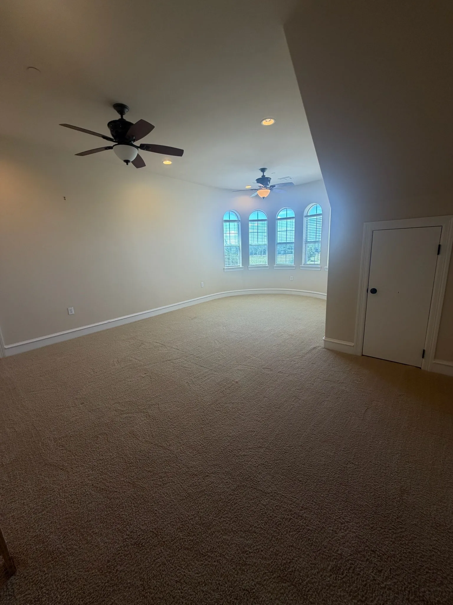 Spacious room featuring multiple arched windows, wall-to-wall carpeting, recessed lighting, and two ceiling fans