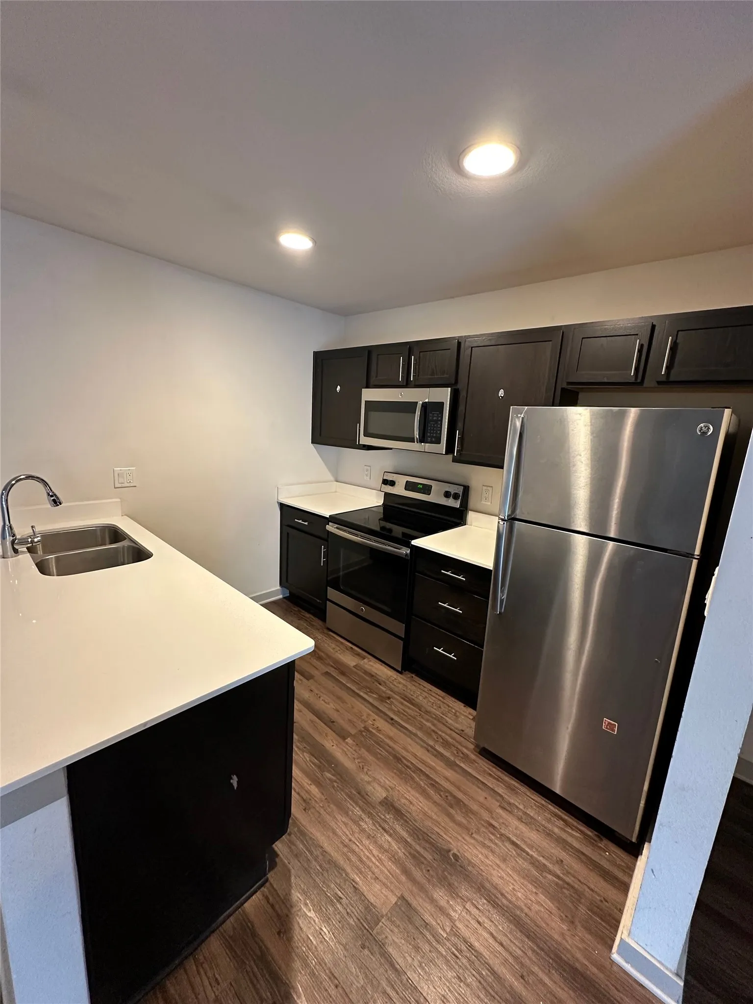 Modern kitchen featuring dark cabinetry, white countertops, stainless steel appliances, and wood-finish flooring