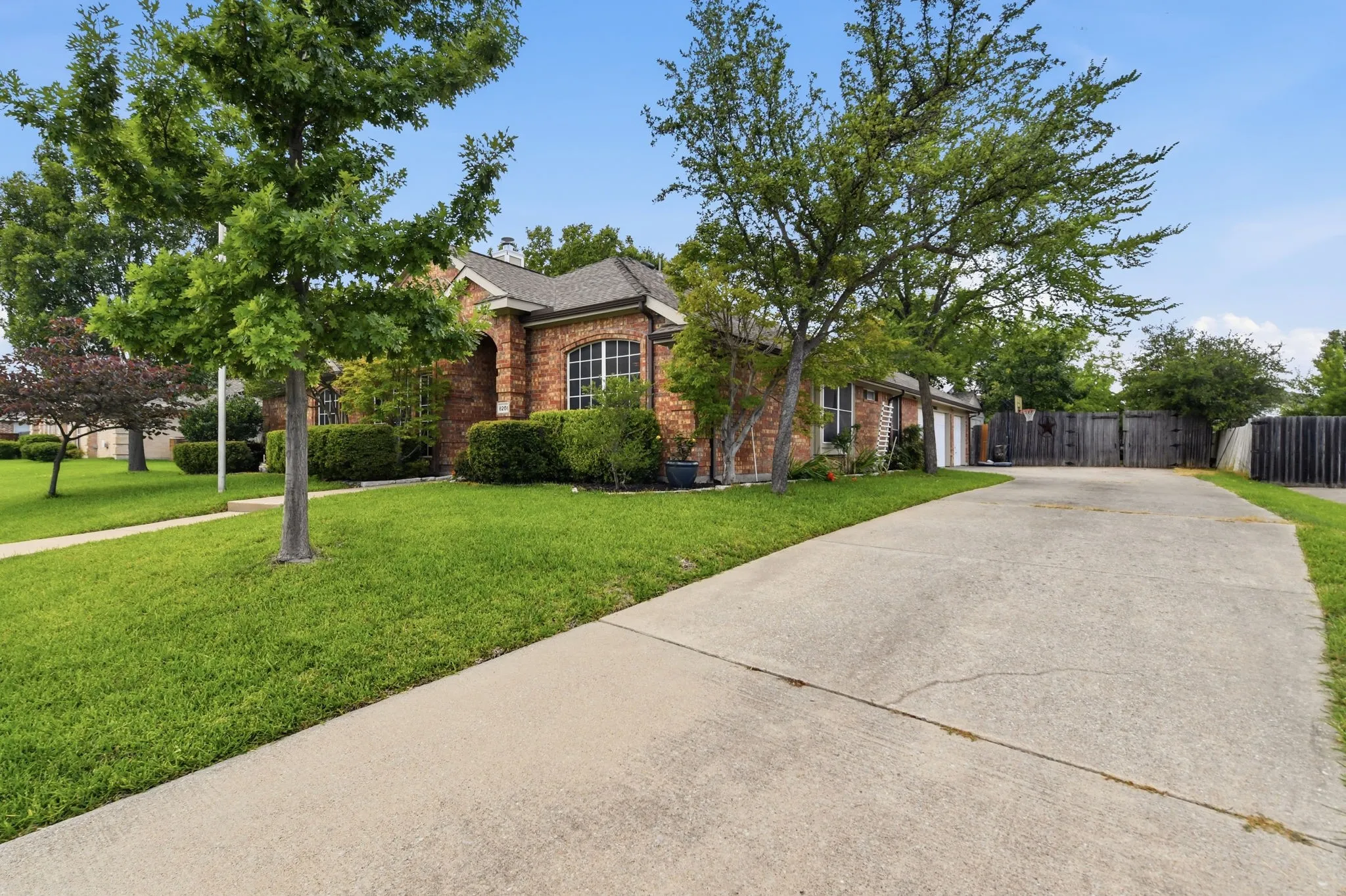 Brick exterior with an arched entryway, multiple windows, an attached garage, a concrete driveway, and mature landscaping