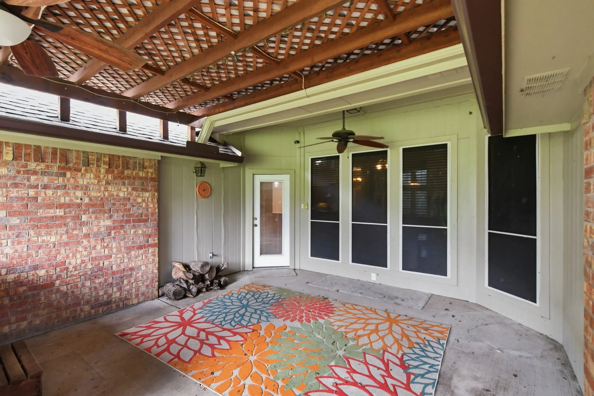 Covered patio featuring a wood lattice ceiling, concrete flooring, and an exterior brick wall