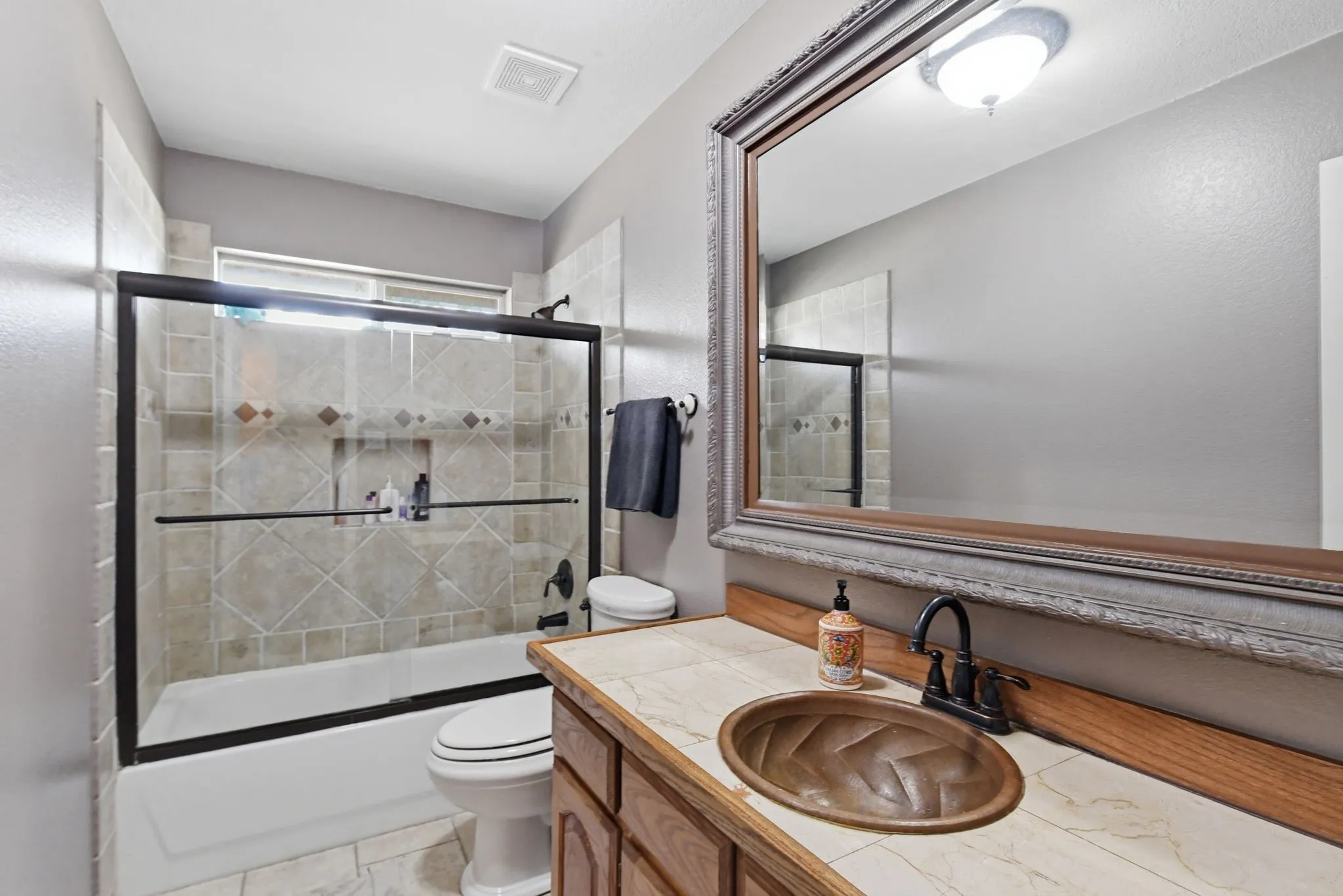 Contemporary bathroom featuring a dark bronze framed shower enclosure over a bathtub, a decorative tile surround with an inset niche, and a window for natural illumination