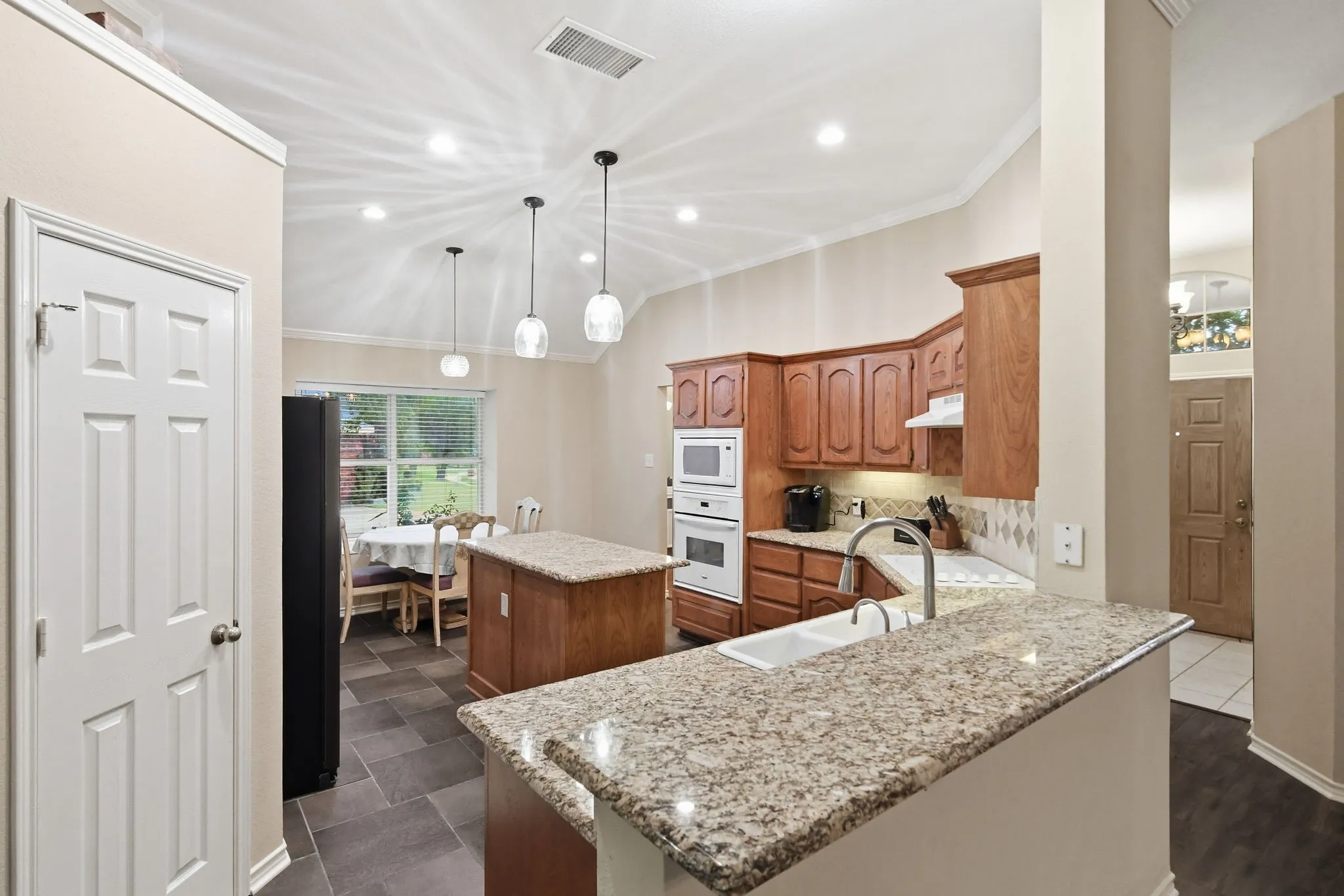 Kitchen featuring a granite-topped island, wood cabinetry, built-in double ovens, and tile flooring