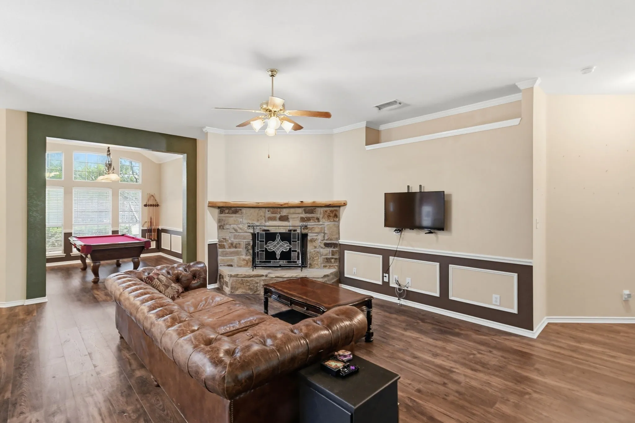 Spacious living area featuring wood-finish flooring, a stone-faced fireplace with a hearth, and a ceiling fan