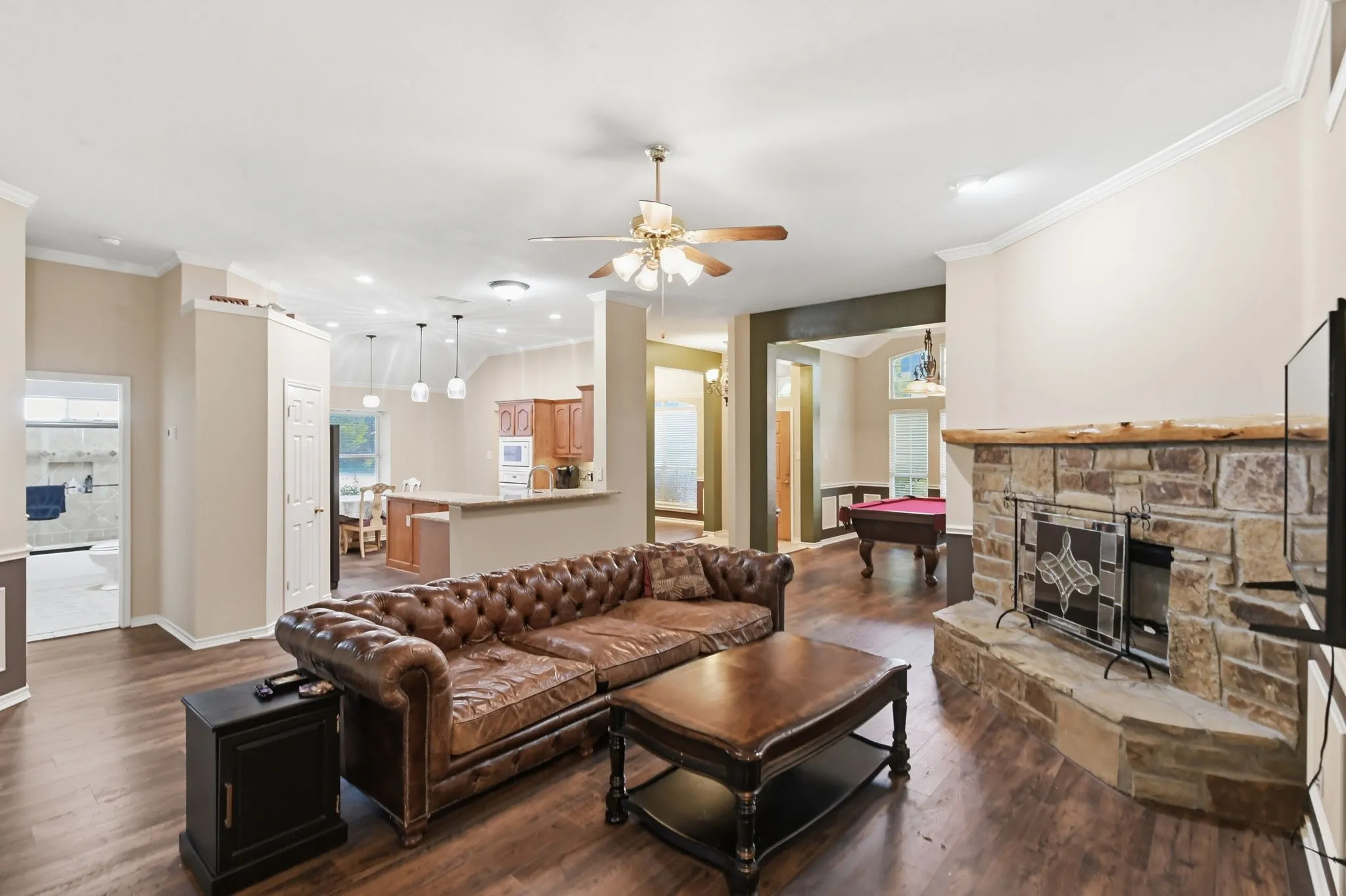 Spacious living area featuring wood-finish flooring, a stone-faced fireplace with a natural wood mantel, and crown molding