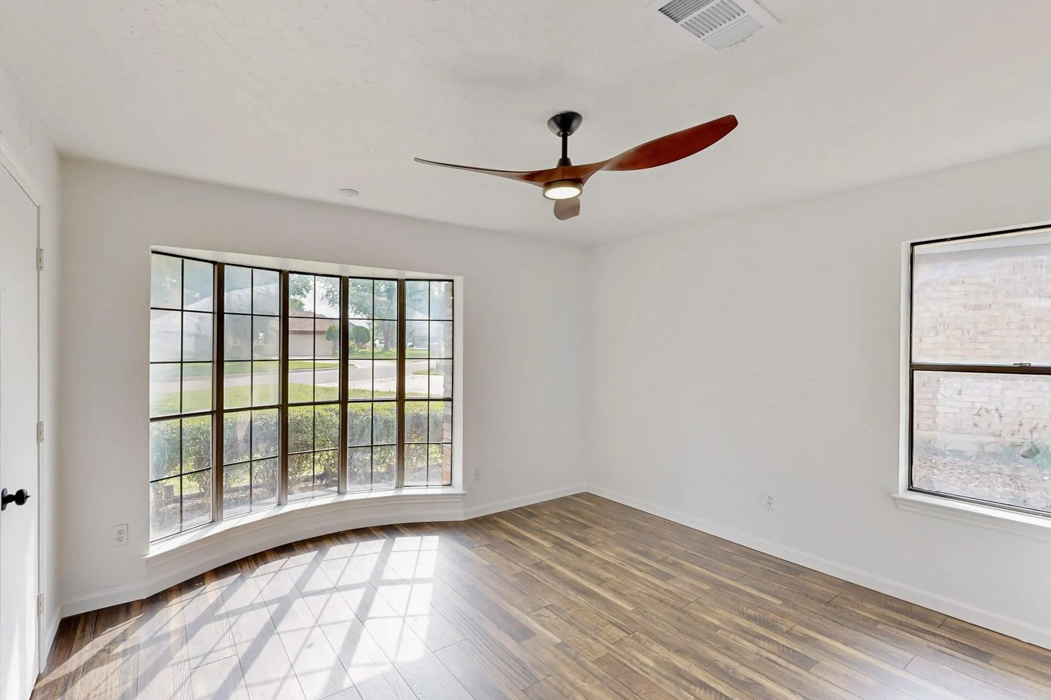Room featuring wood-finish flooring, a large bowed window with grids, and a modern ceiling fan with integrated lighting