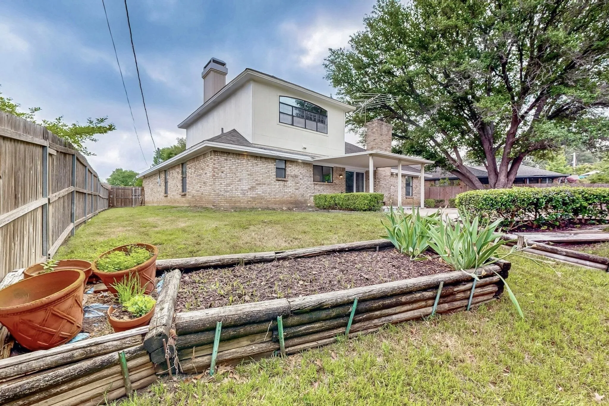 Expansive backyard featuring a wood fence, mature trees, a covered patio, and a raised garden bed