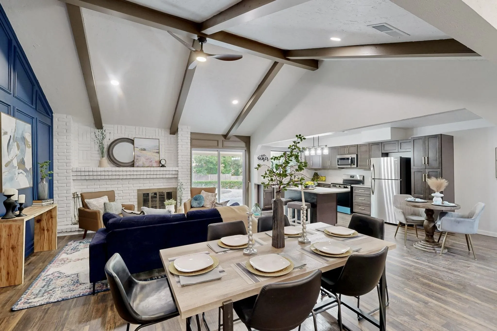 Open-concept living space featuring vaulted ceilings with exposed beams, wood-finish flooring, and a white brick fireplace