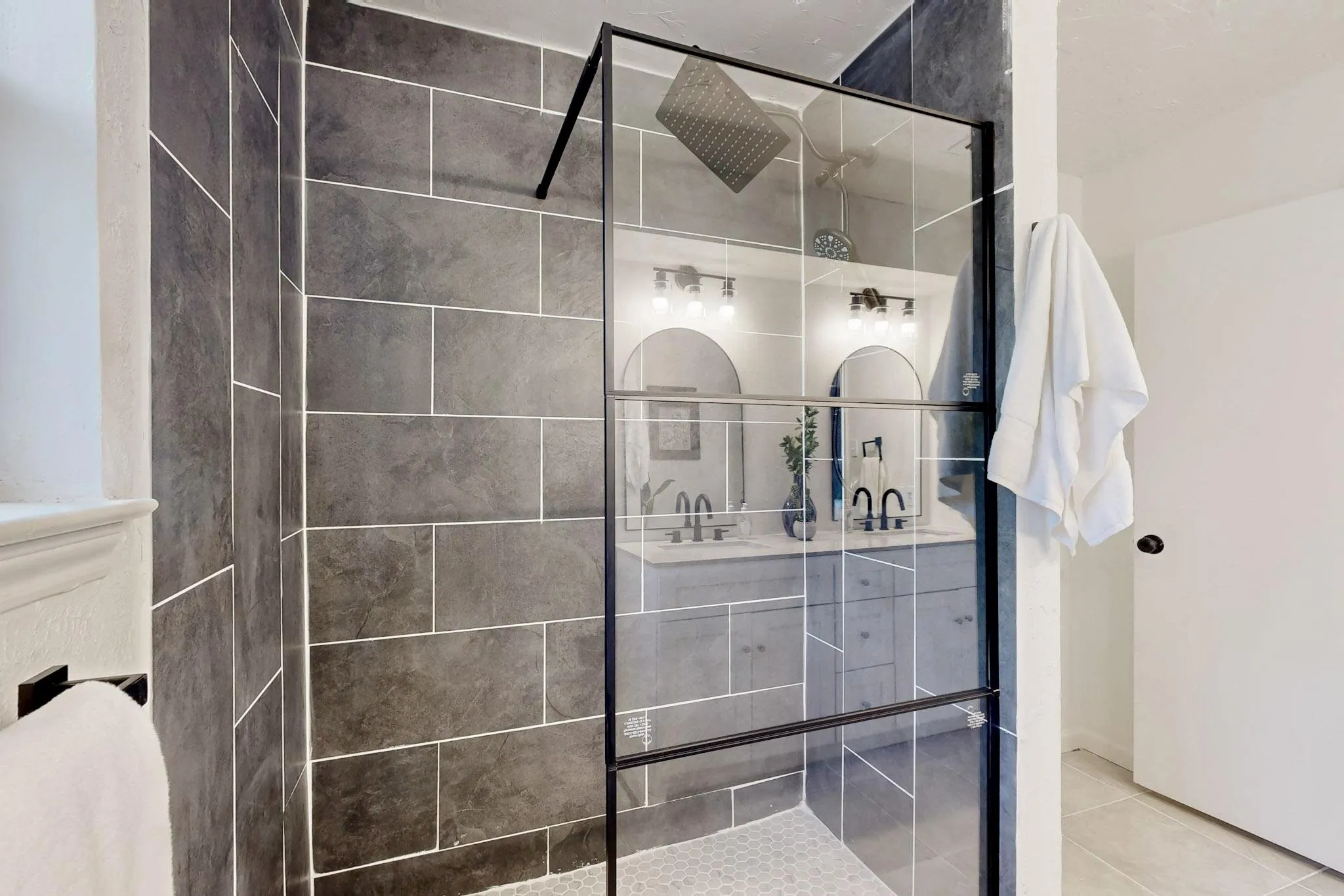 Walk-in shower with dark rectangular tile walls and a hexagonal tile floor