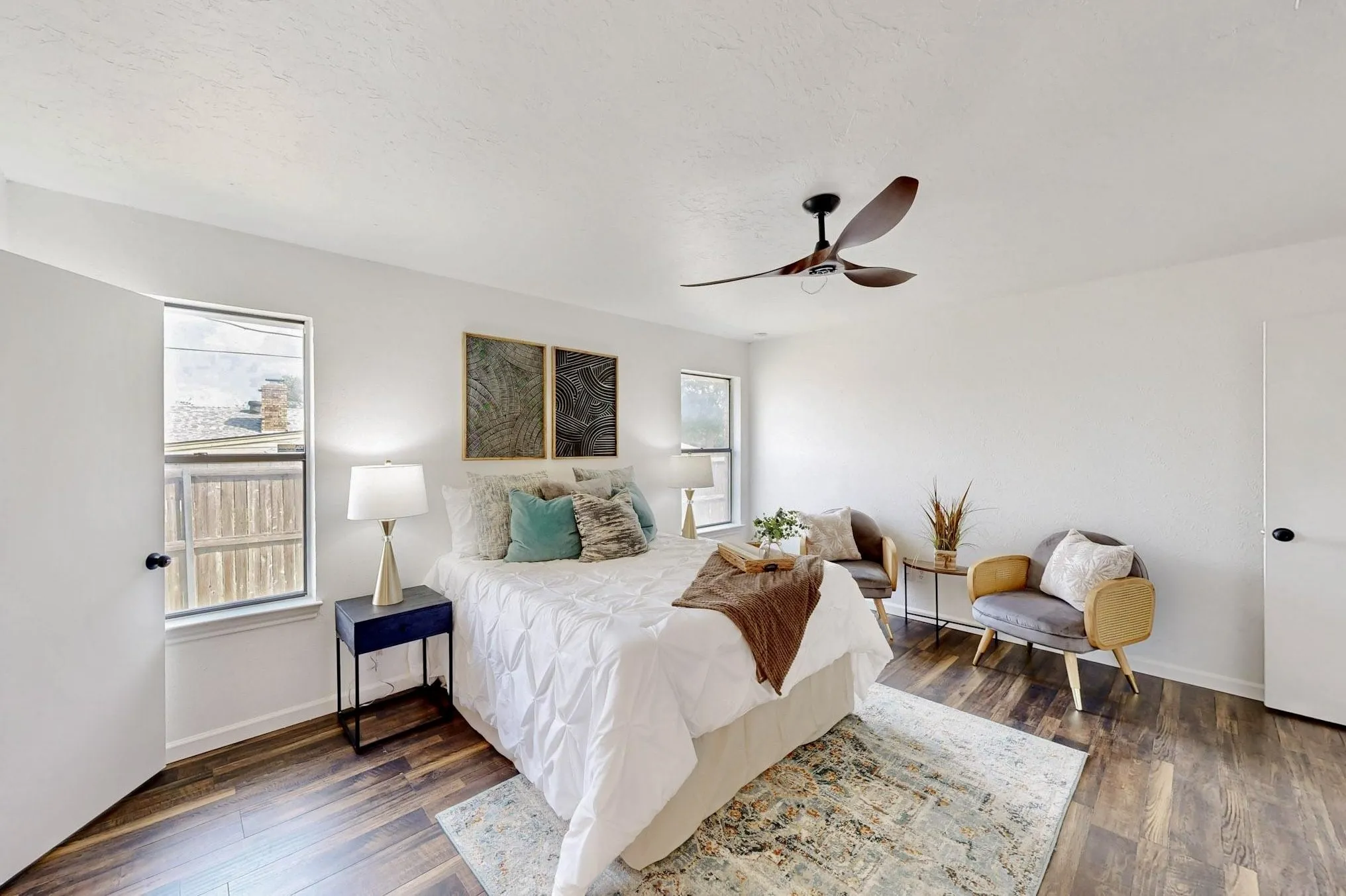 Spacious room featuring wood-finish flooring, white painted walls, and a ceiling fan with dark blades