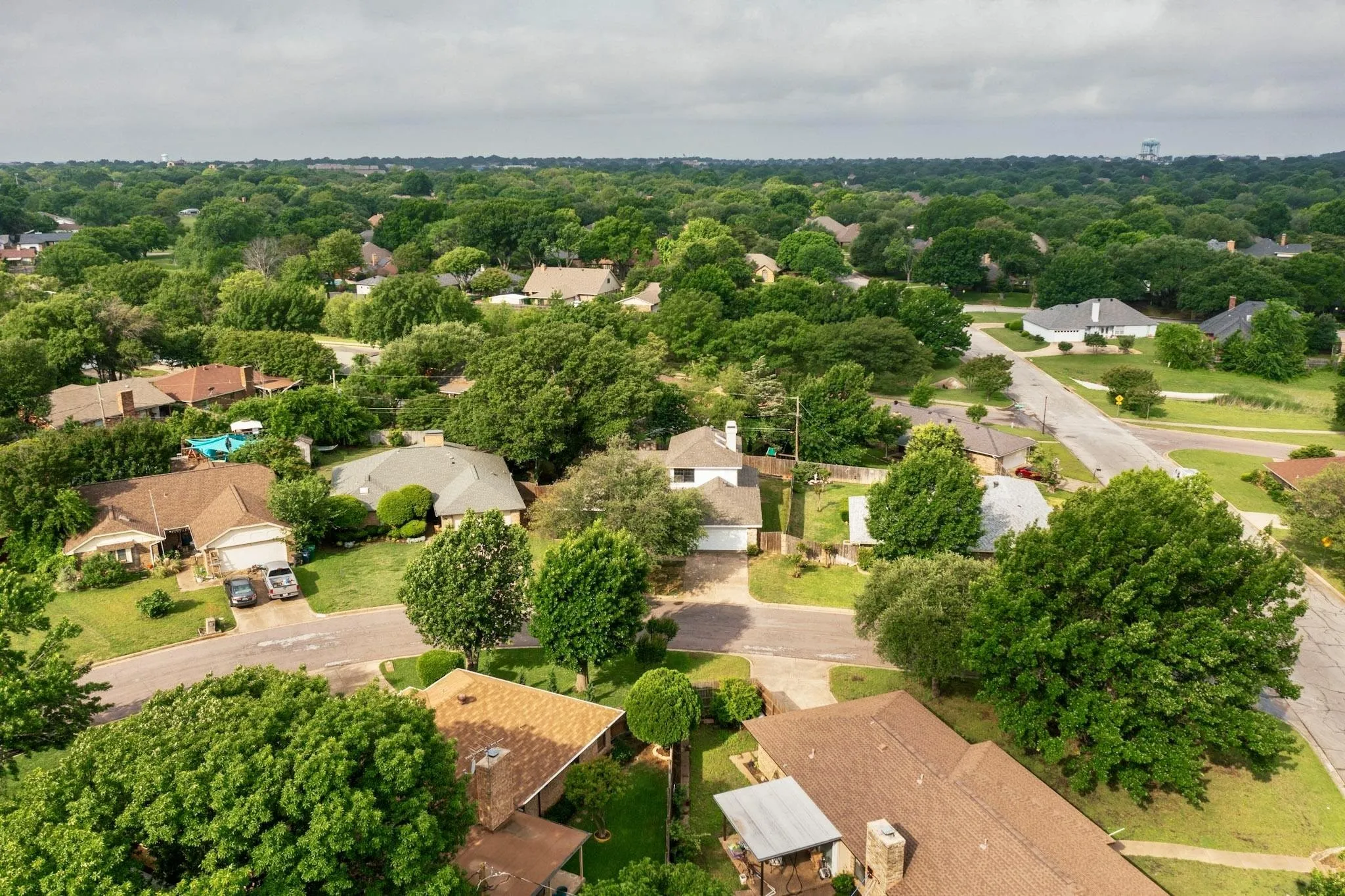 Residential neighborhood featuring mature tree canopy, varied single-family homes, paved streets, and a distant water tower