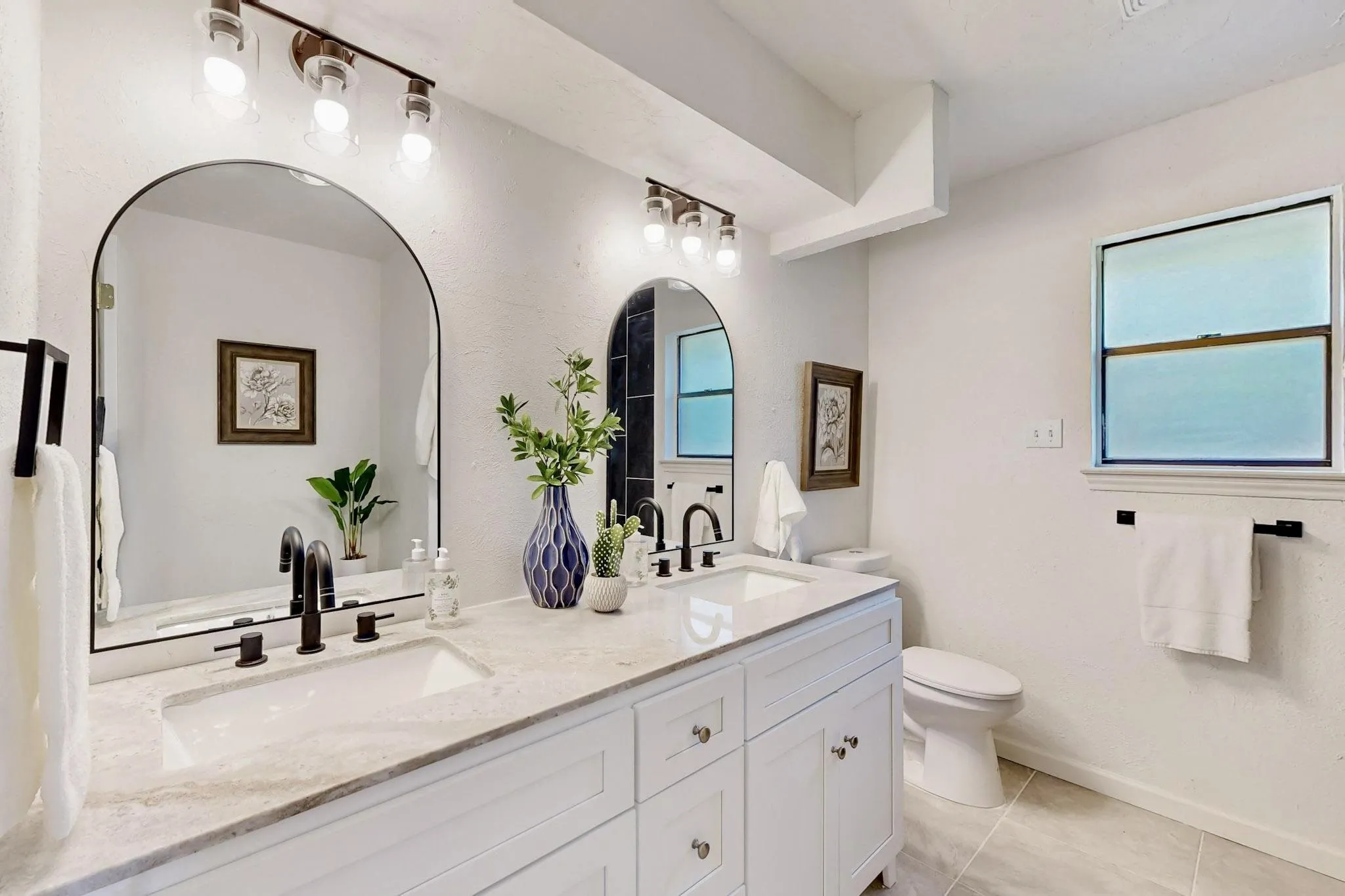 Double vanity featuring two integrated sinks set in a light-toned countertop, complemented by dual arched mirrors with matte black frames