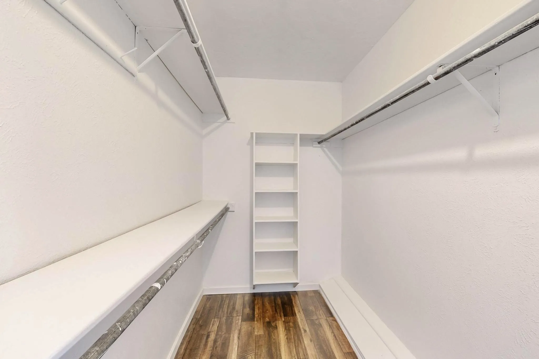 Walk-in closet featuring wood-finish flooring, white walls, built-in shelving, and dual clothing rods with overhead shelving