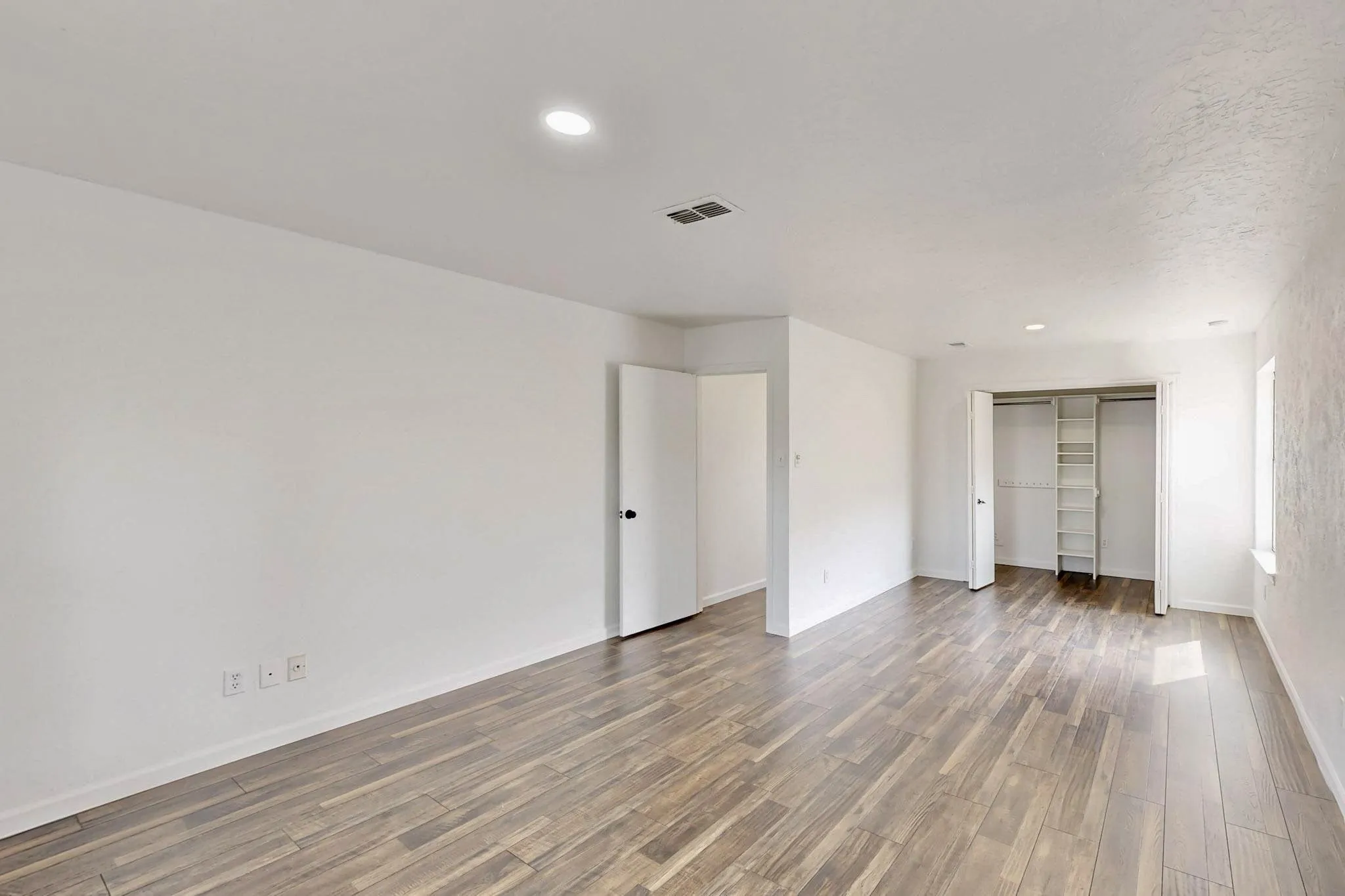 Spacious room with wood-finish flooring, recessed lighting, and white walls