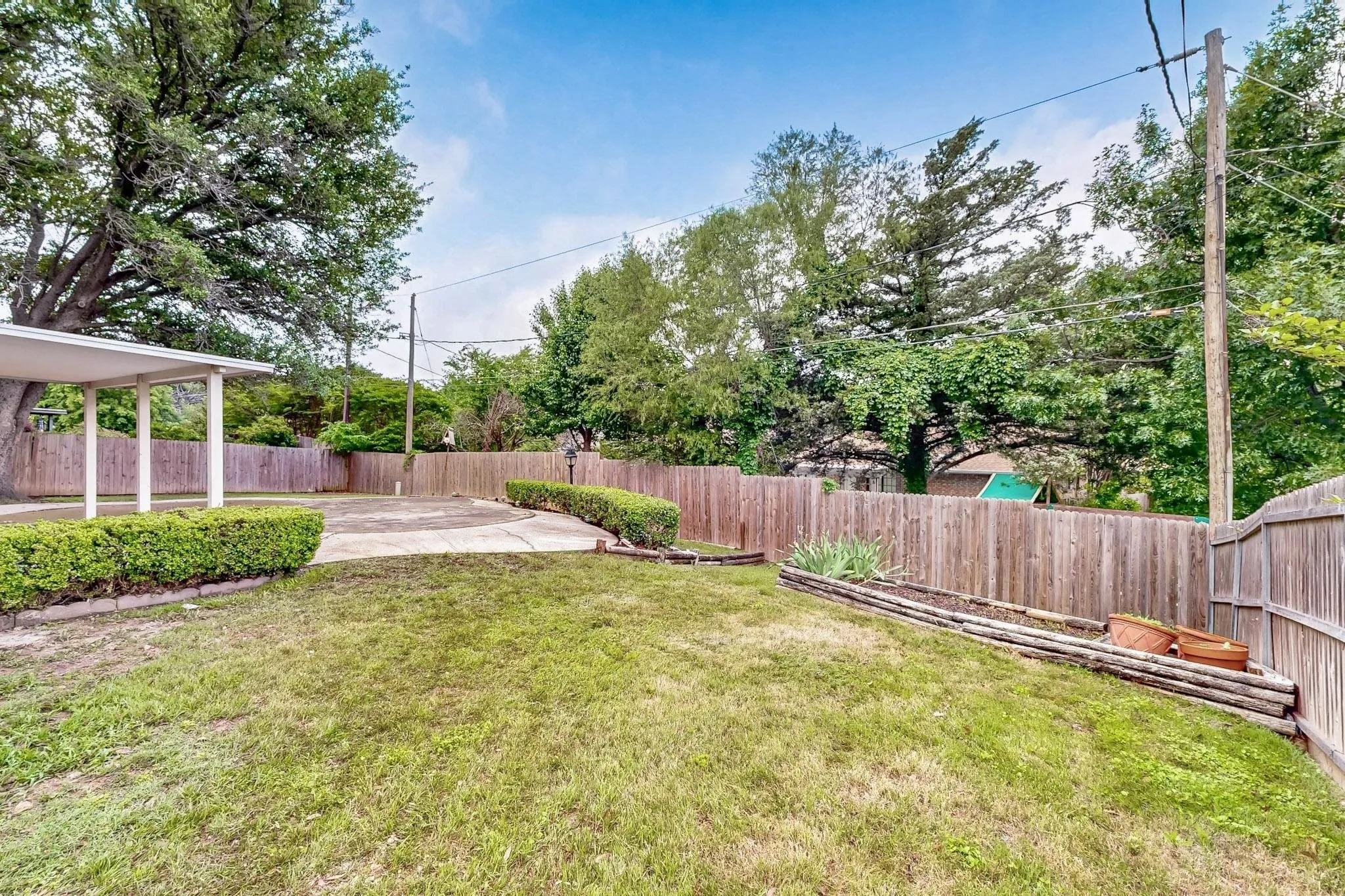 Expansive backyard featuring a manicured lawn, established privacy fencing, mature trees, and a covered patio area
