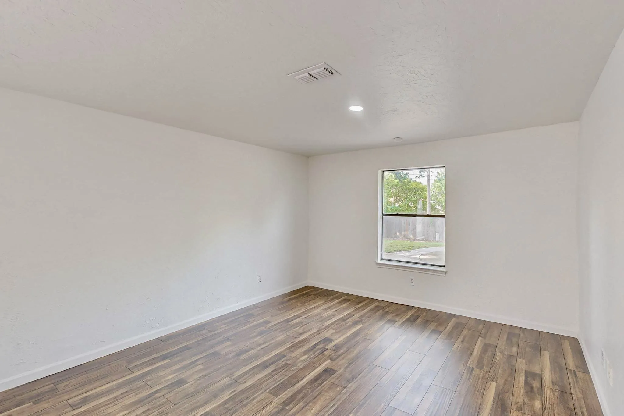 Interior room featuring wood-finish flooring, white painted walls, and a single window with white trim