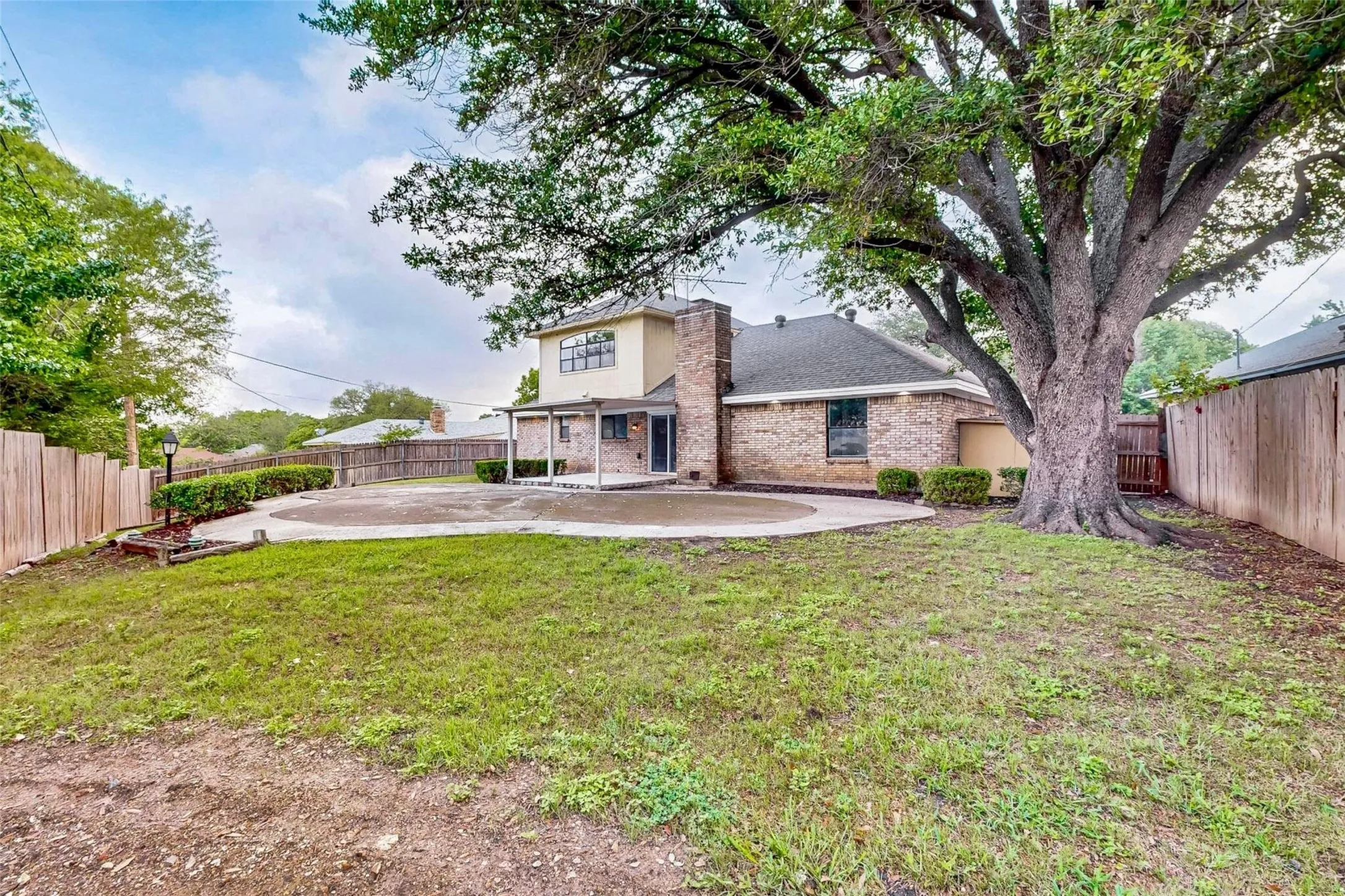 Expansive backyard featuring a large tree, a brick and stucco exterior, a covered patio, and a privacy fence