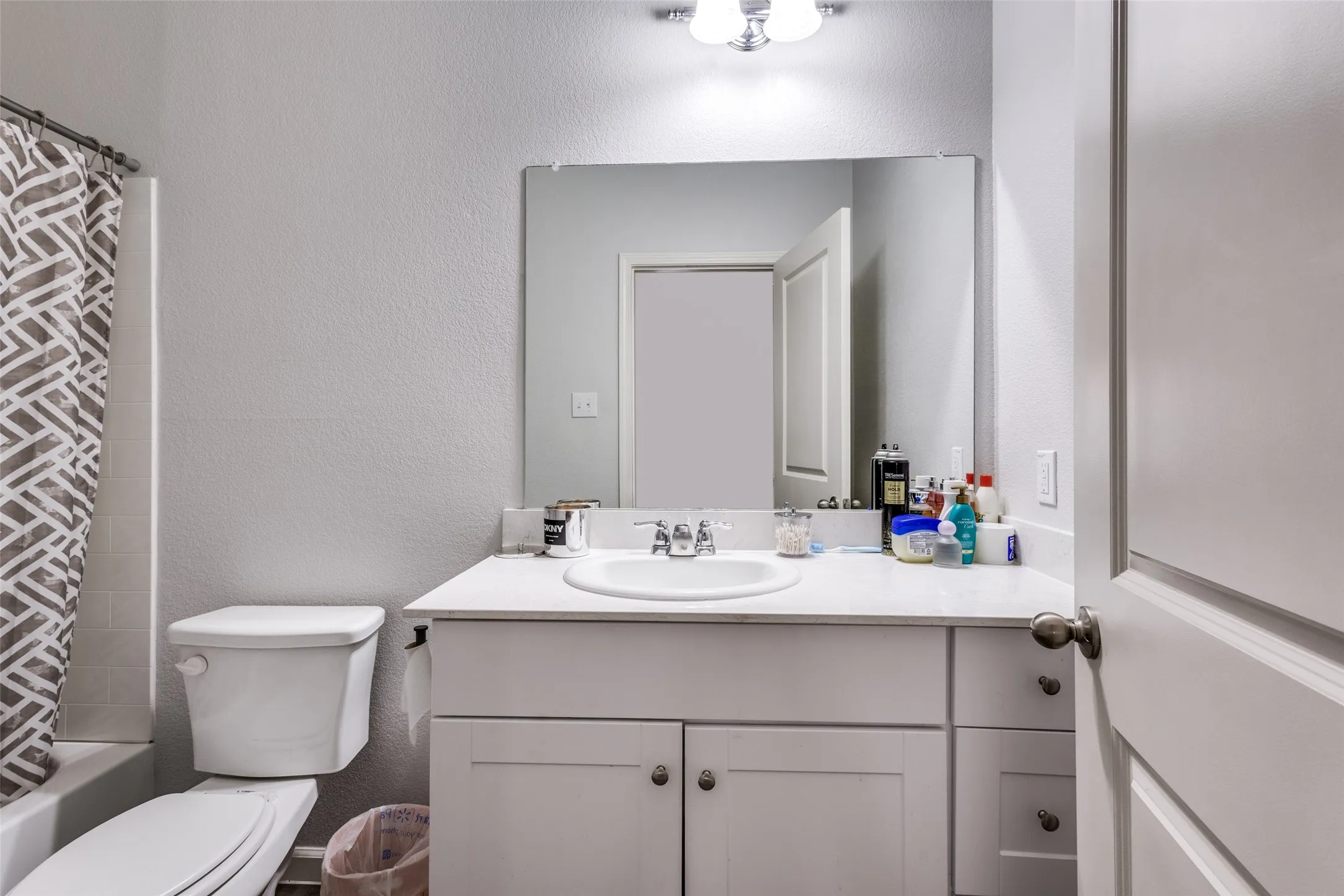 Bathroom featuring a white vanity with integrated sink, a large wall-mounted mirror, brushed nickel hardware, and a tub with tiled surround