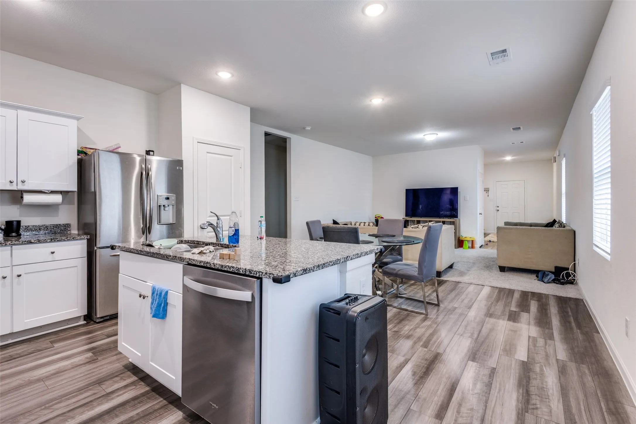Open-concept living space featuring a kitchen island with stone countertops, stainless steel appliances, white cabinetry, recessed lighting, and wood-finish flooring