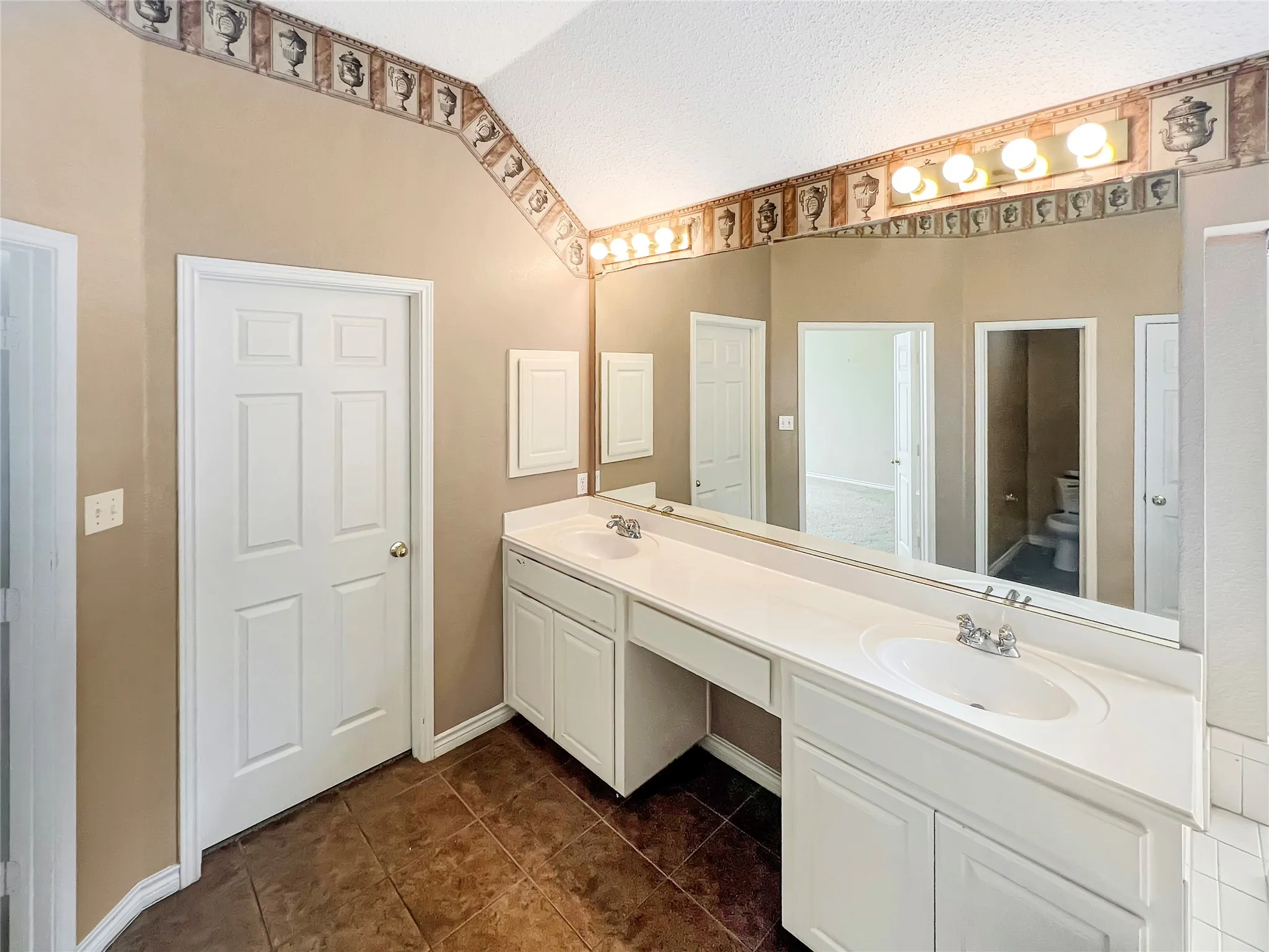 Bathroom vanity featuring dual sinks, white cabinetry, a built-in dressing area, and a large wall-mounted mirror