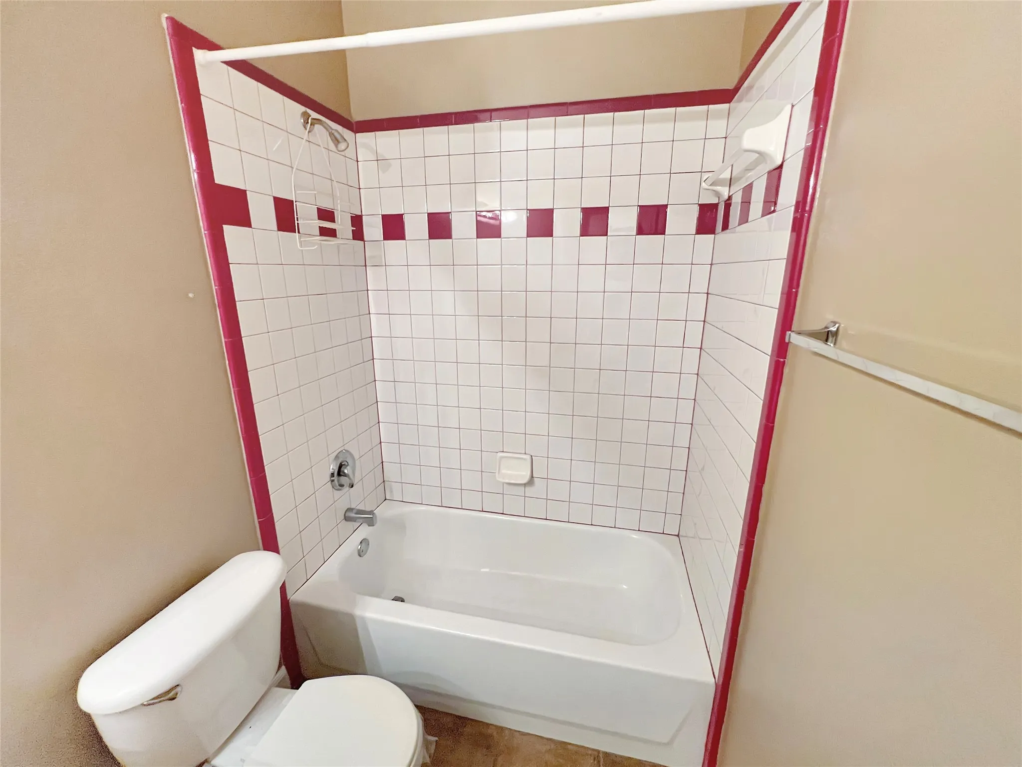 Tub and shower combination featuring white square tiles with a red accent band