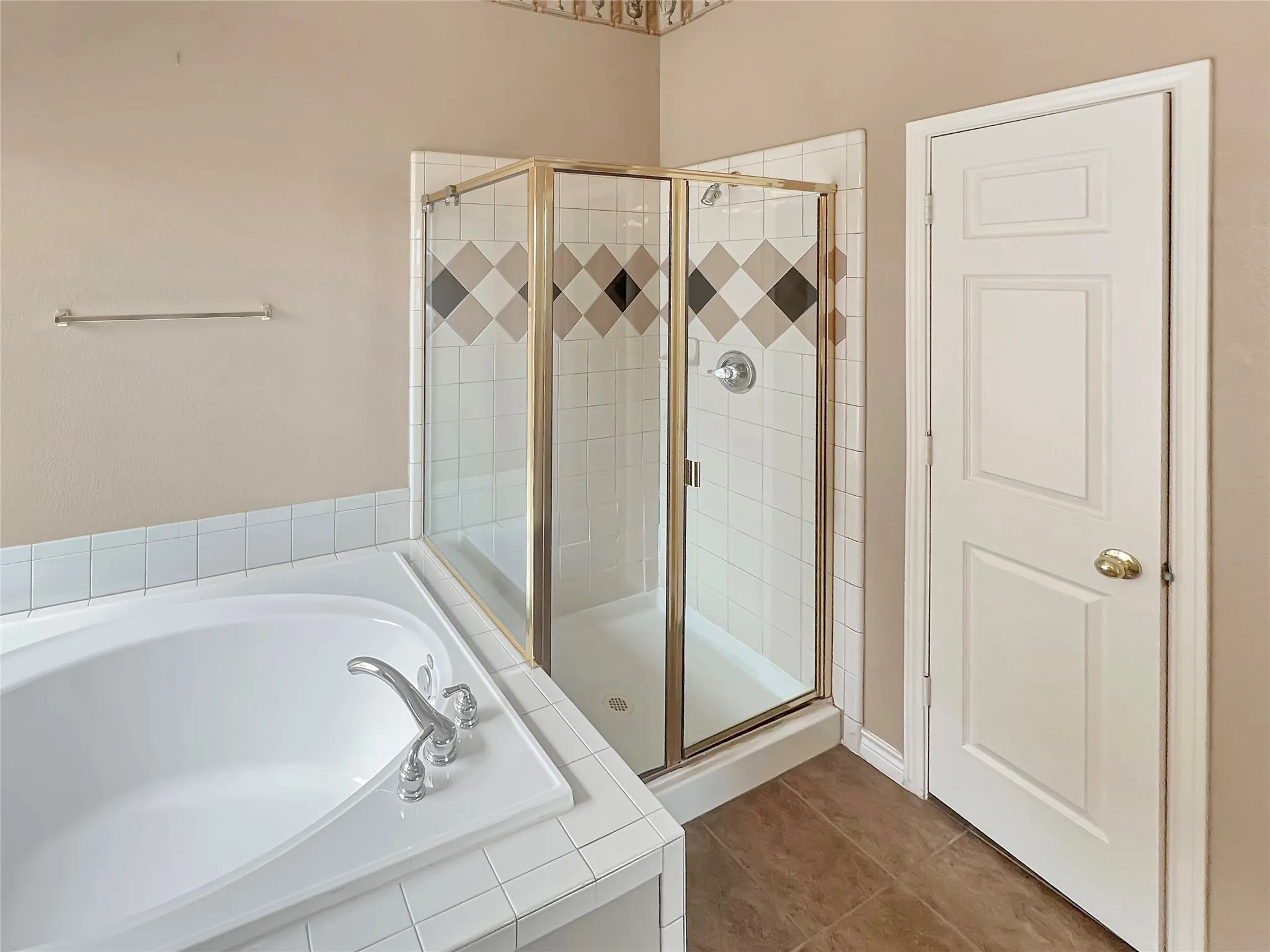 Built-in tub with chrome fixtures, enclosed shower with gold-tone frame, decorative tile accents, and neutral wall tones