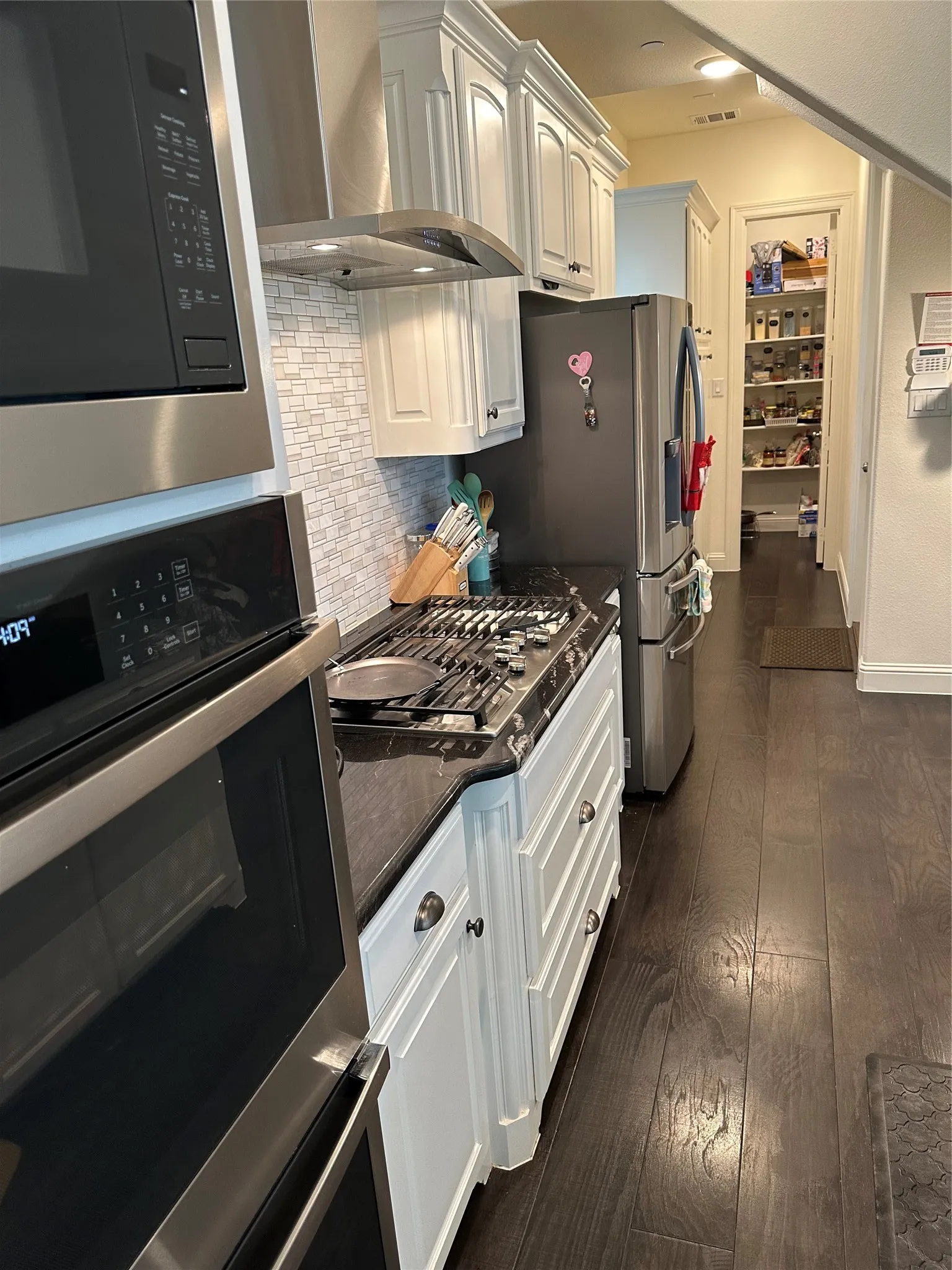 Kitchen featuring stainless steel appliances, white cabinetry, dark stone countertops, a tile backsplash, and dark wood-finish flooring