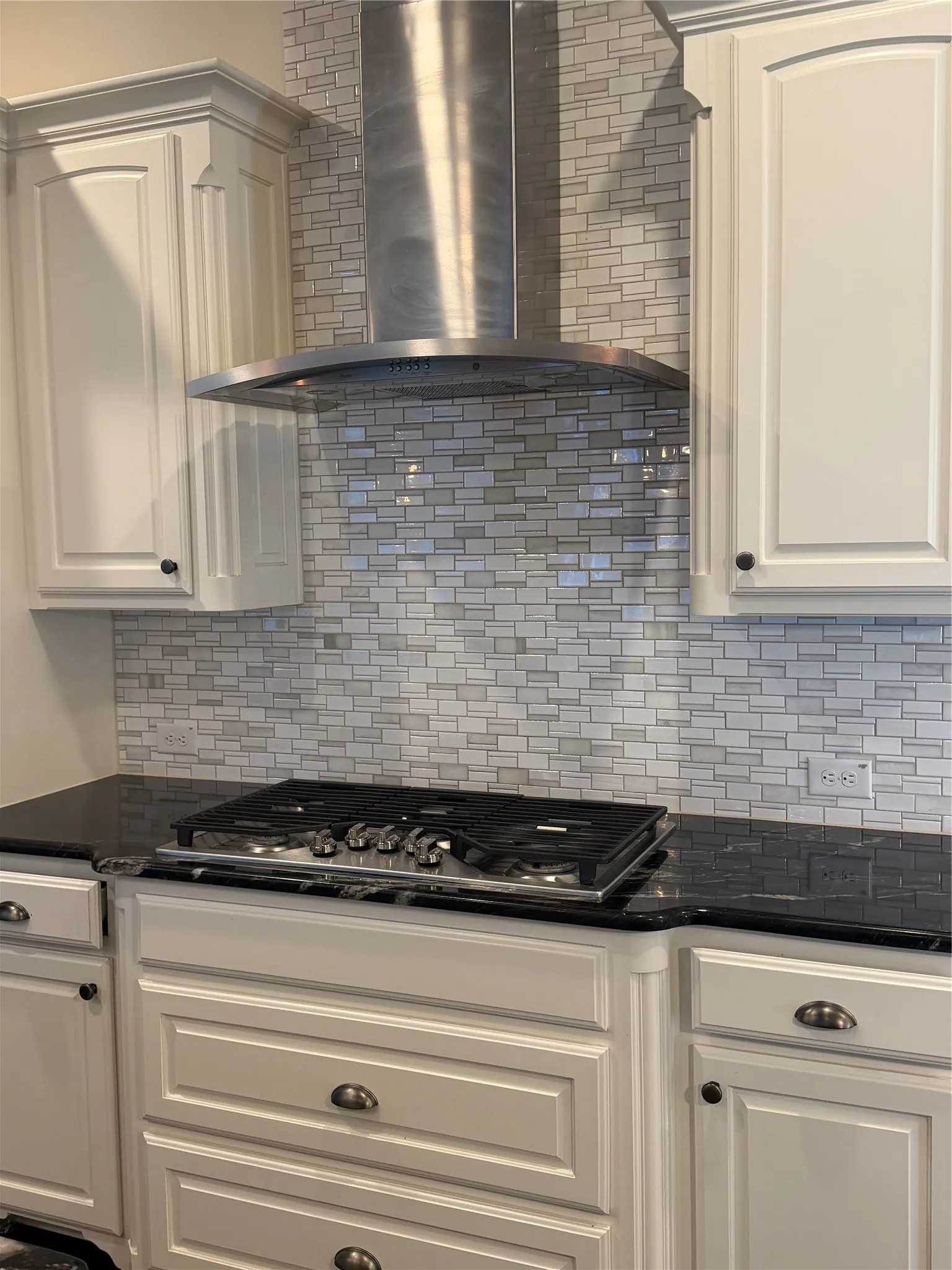 White cabinetry, dark stone countertops, mosaic tile backsplash, stainless steel range hood, and built-in gas range