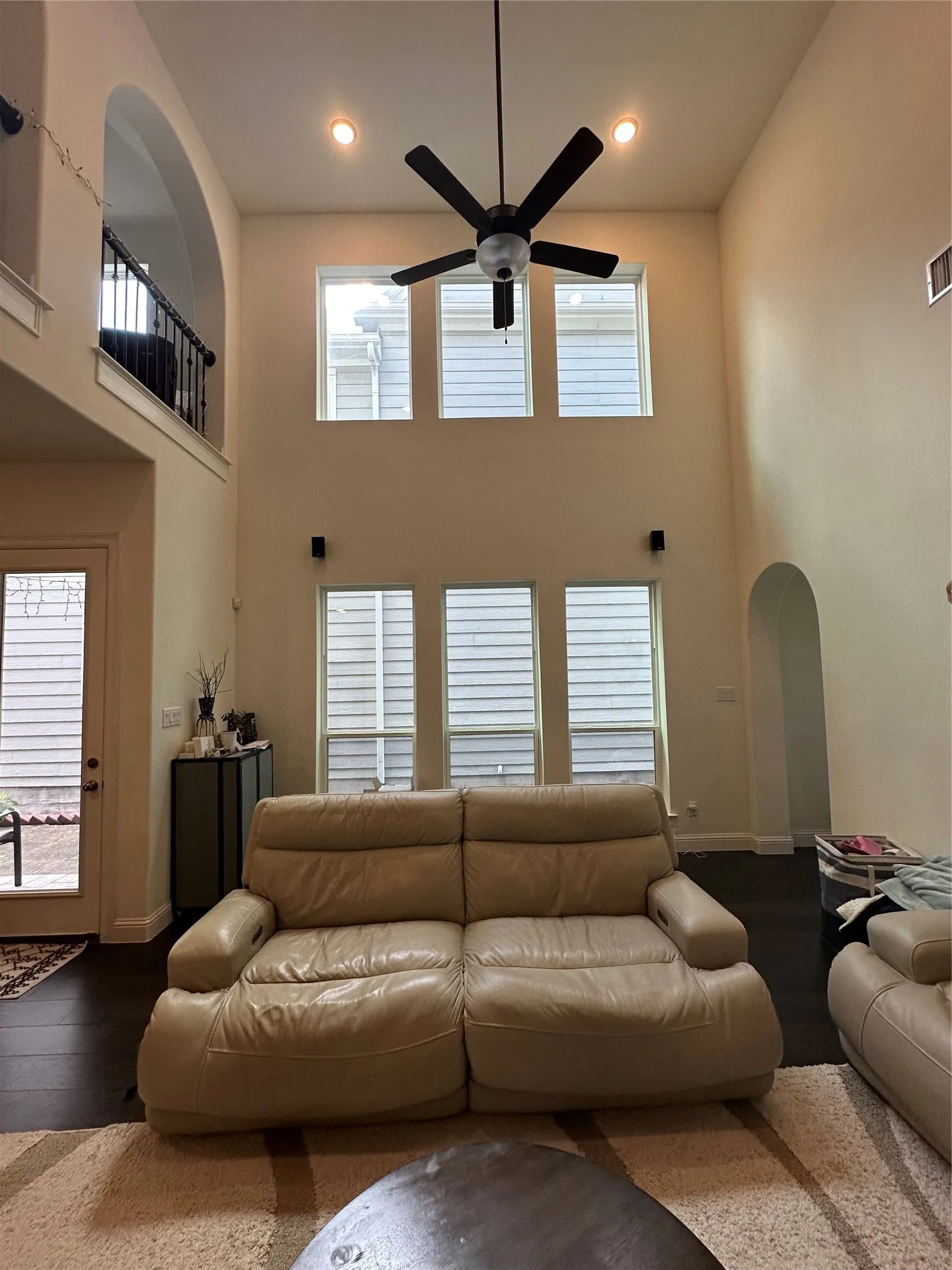Two-story living area featuring dark wood-finish flooring, a contemporary ceiling fan, recessed lighting, and a series of six large windows across two levels