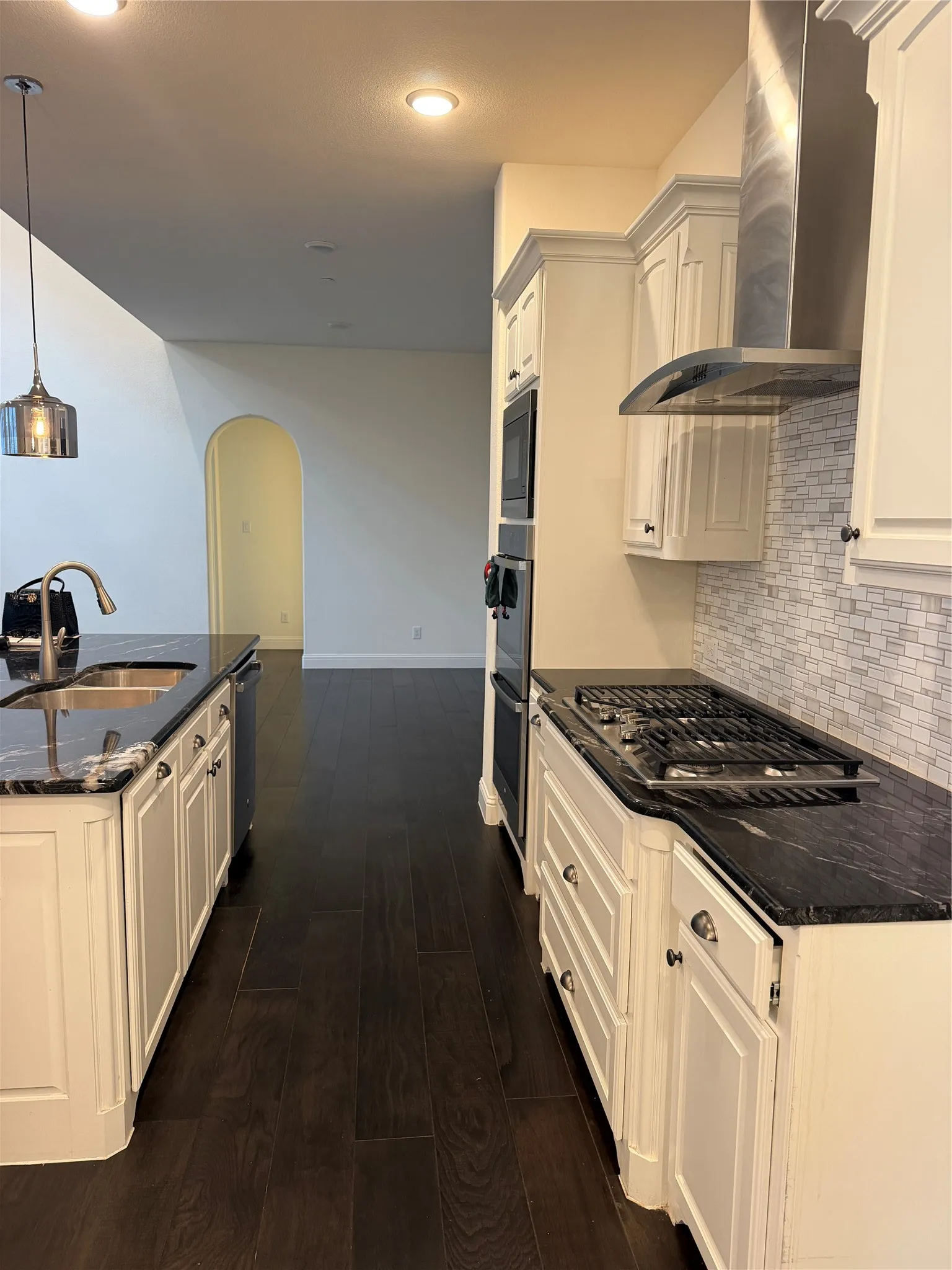 Kitchen featuring dark wood-finish flooring, white cabinetry, dark stone countertops, and a stainless steel gas range with a matching range hood