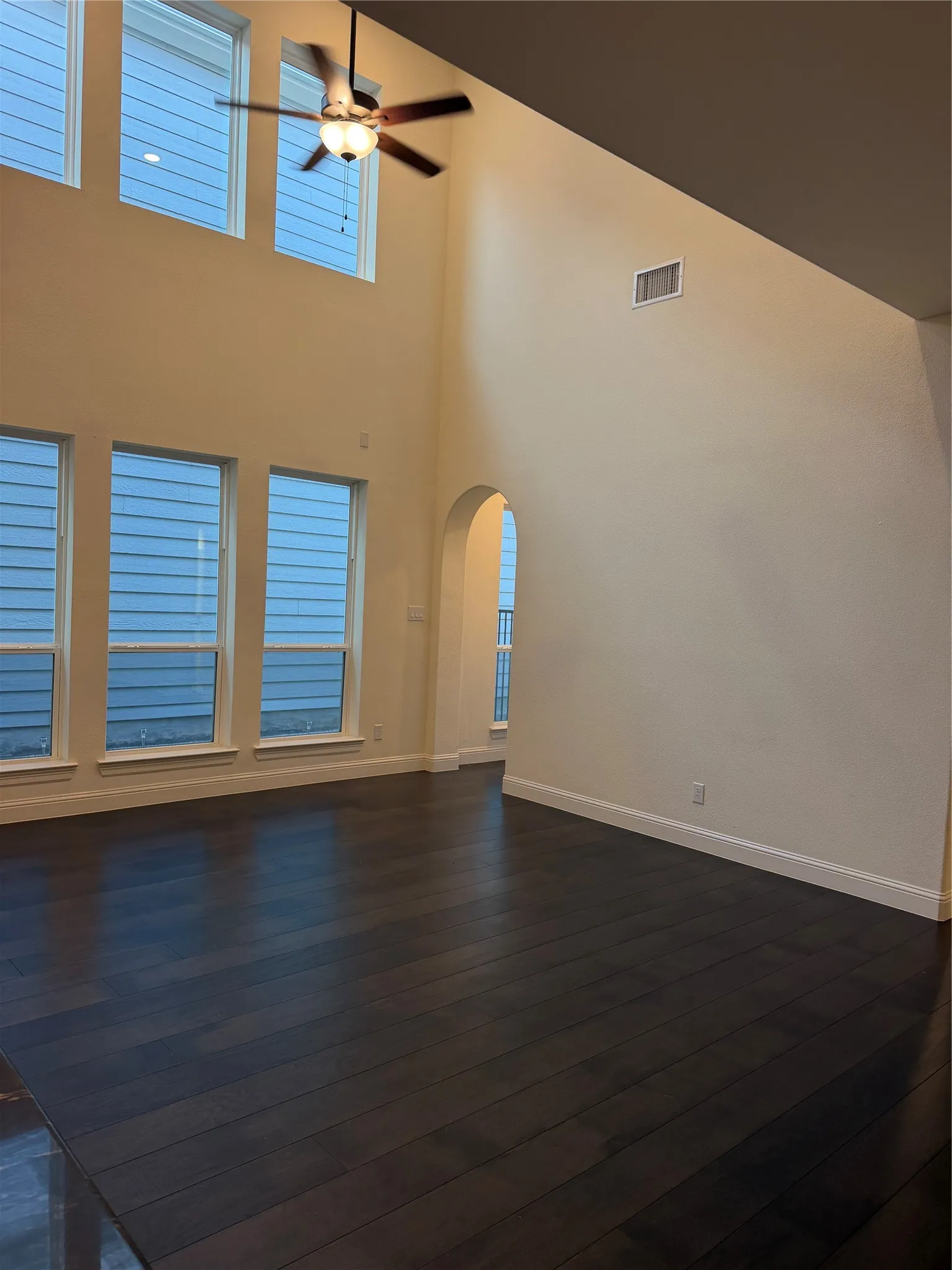 High ceilings with a ceiling fan, dark wood-finish flooring, multiple windows, and an arched doorway