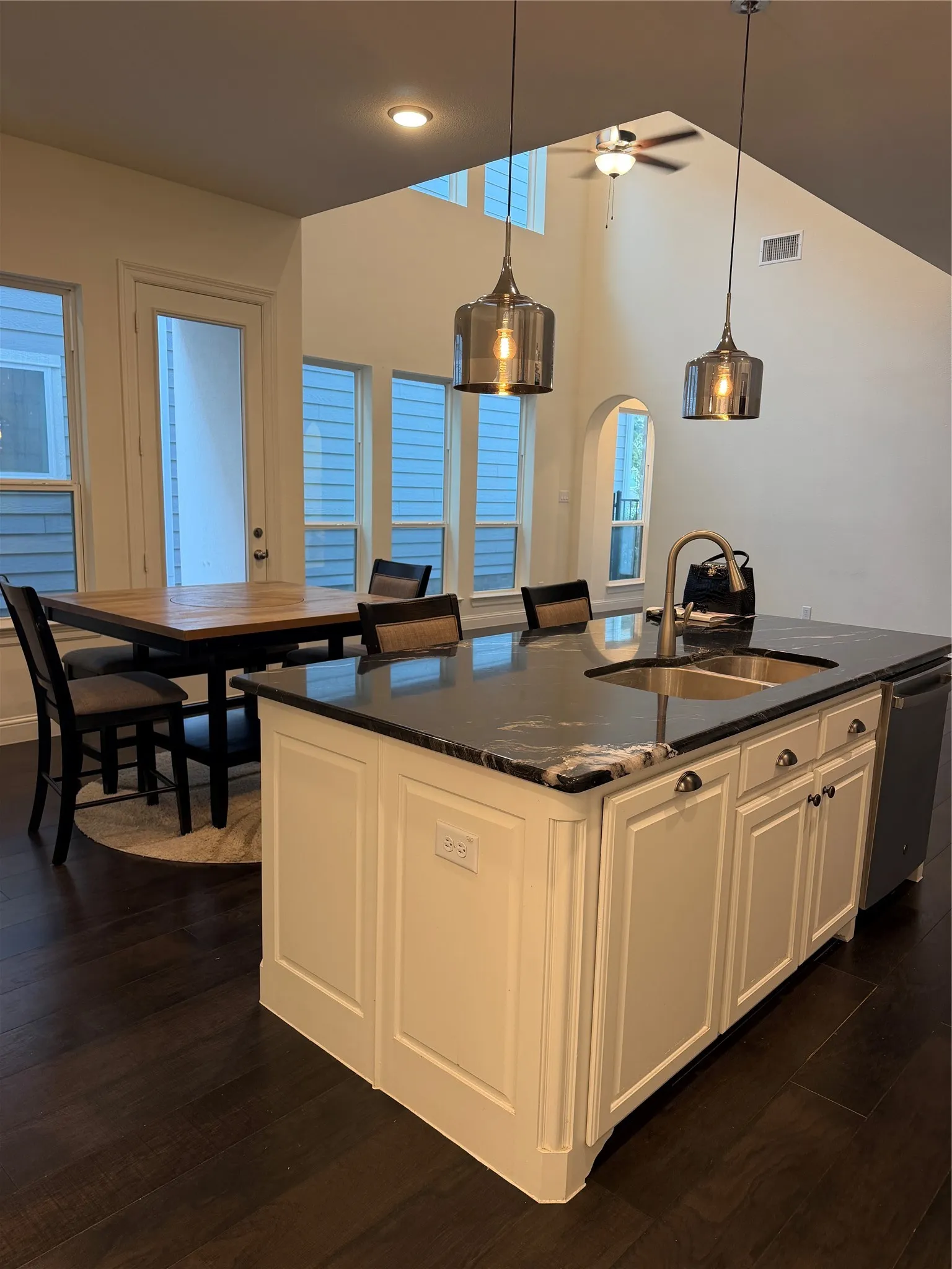 Kitchen island featuring a double-basin sink, dark stone countertop, and white cabinetry