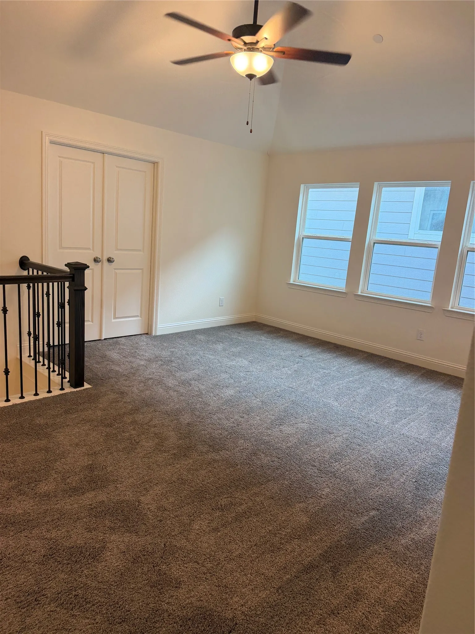 Loft area featuring vaulted ceilings, a ceiling fan with integrated lighting, multiple windows, plush carpeting, and white panel doors