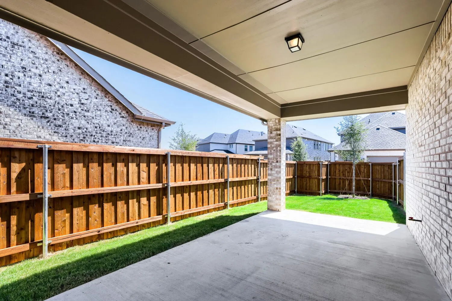 Covered concrete patio extending to a fenced backyard with a manicured lawn