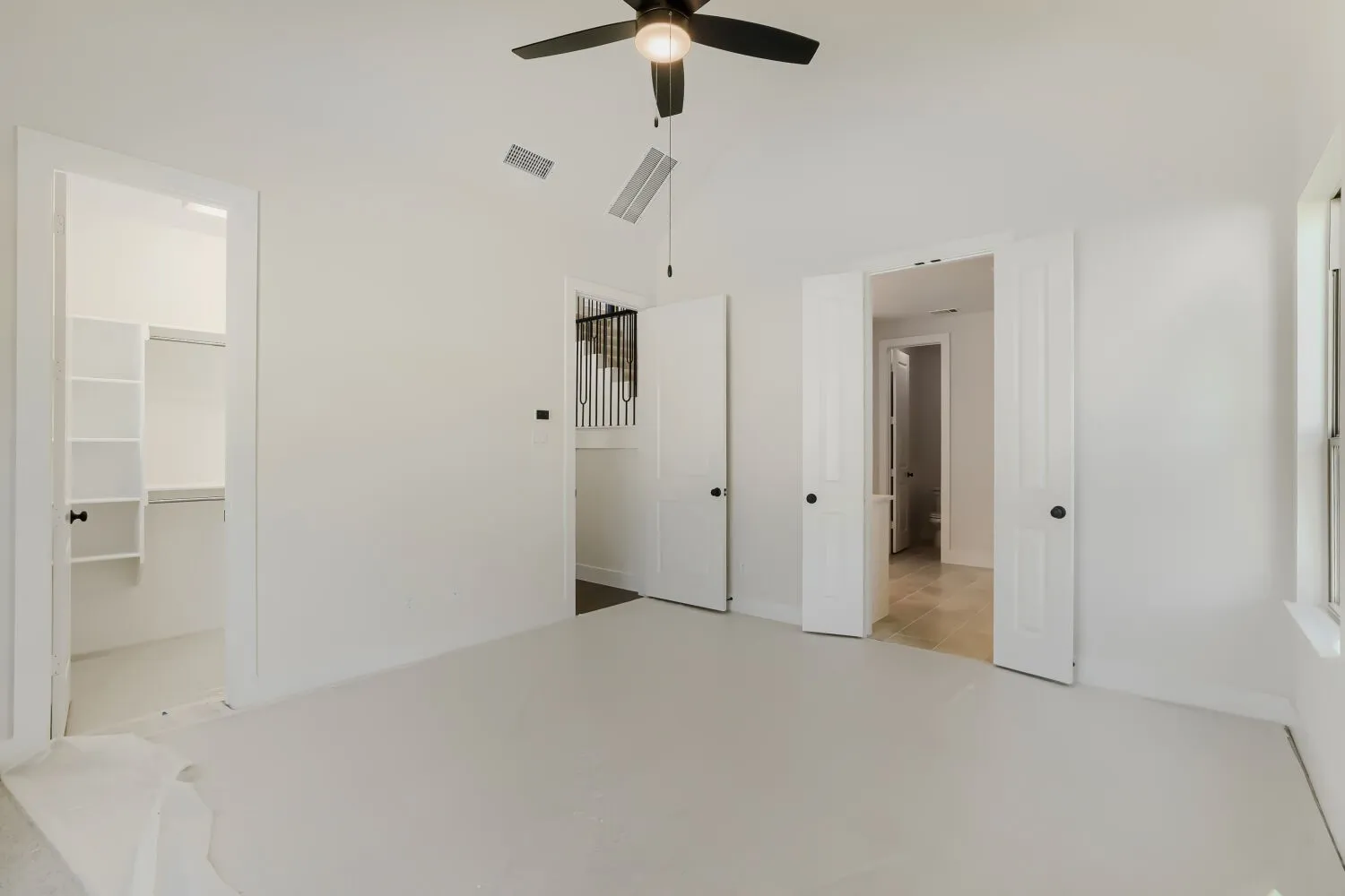 Spacious room featuring a ceiling fan with light fixture, light-toned flooring, white walls, and a window providing natural light