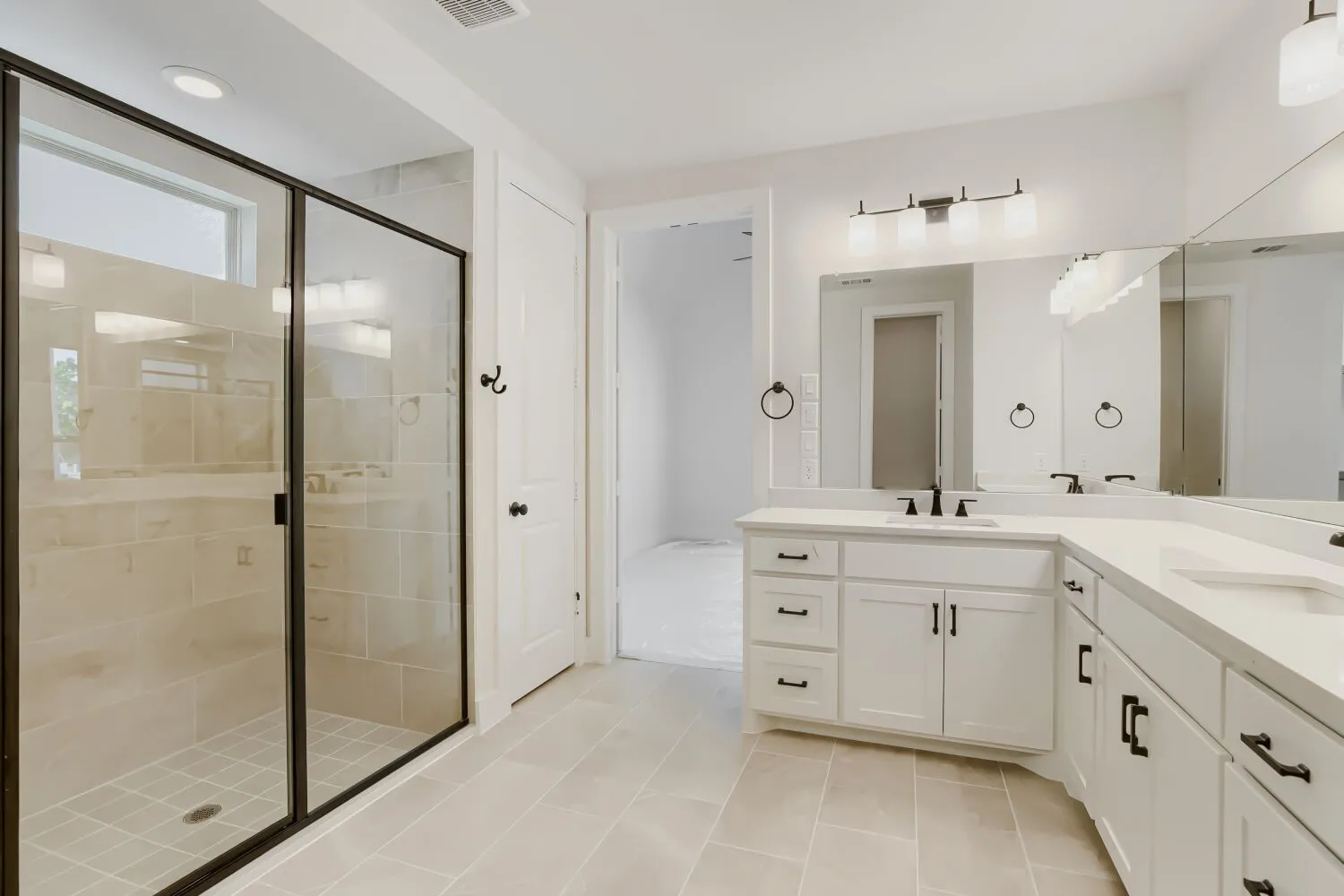 Spacious bathroom featuring a frameless glass shower enclosure with tile surround, dual vanities with white cabinetry and integrated sinks, and ample wall mirrors