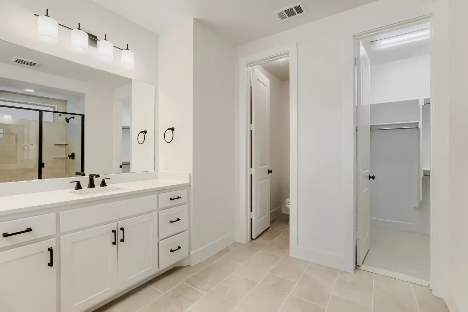 Spacious bathroom featuring a double vanity with white cabinetry, matte black hardware, and an expansive mirror