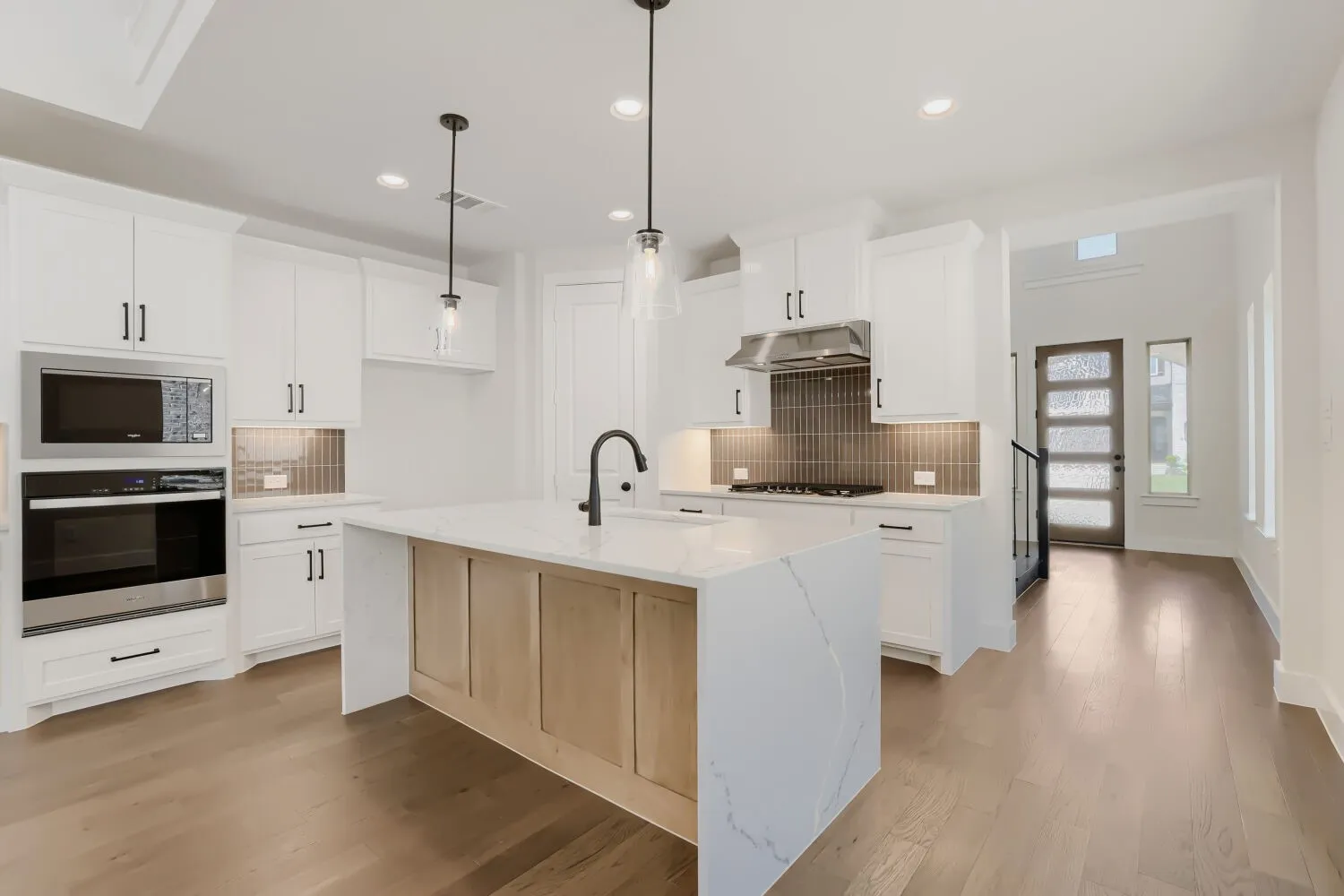 Modern kitchen featuring a waterfall island with wood-finish paneling, white cabinetry, integrated stainless steel appliances, and wood-finish flooring