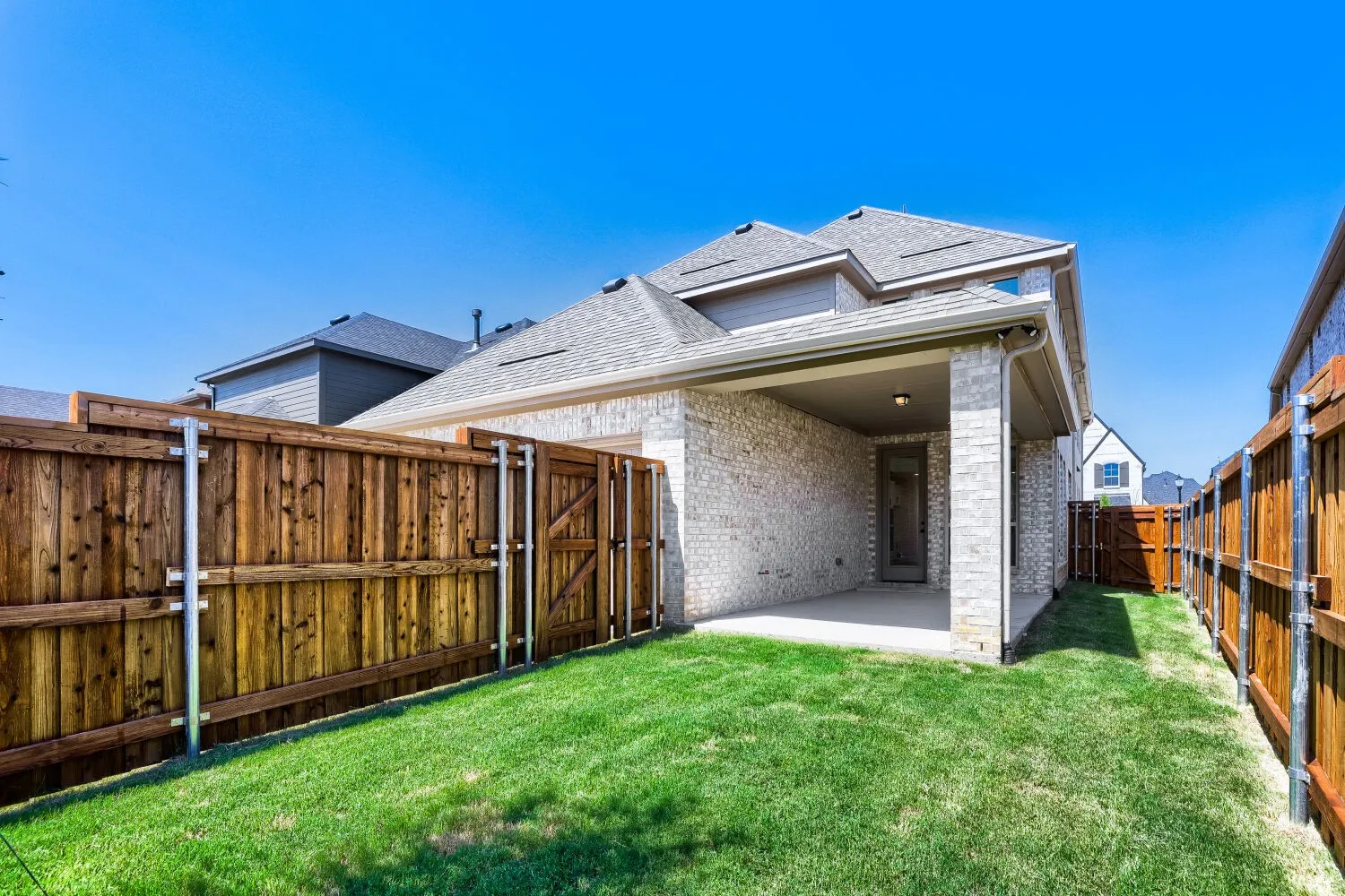 Backyard featuring a covered patio, manicured lawn, and wood privacy fencing with a gate