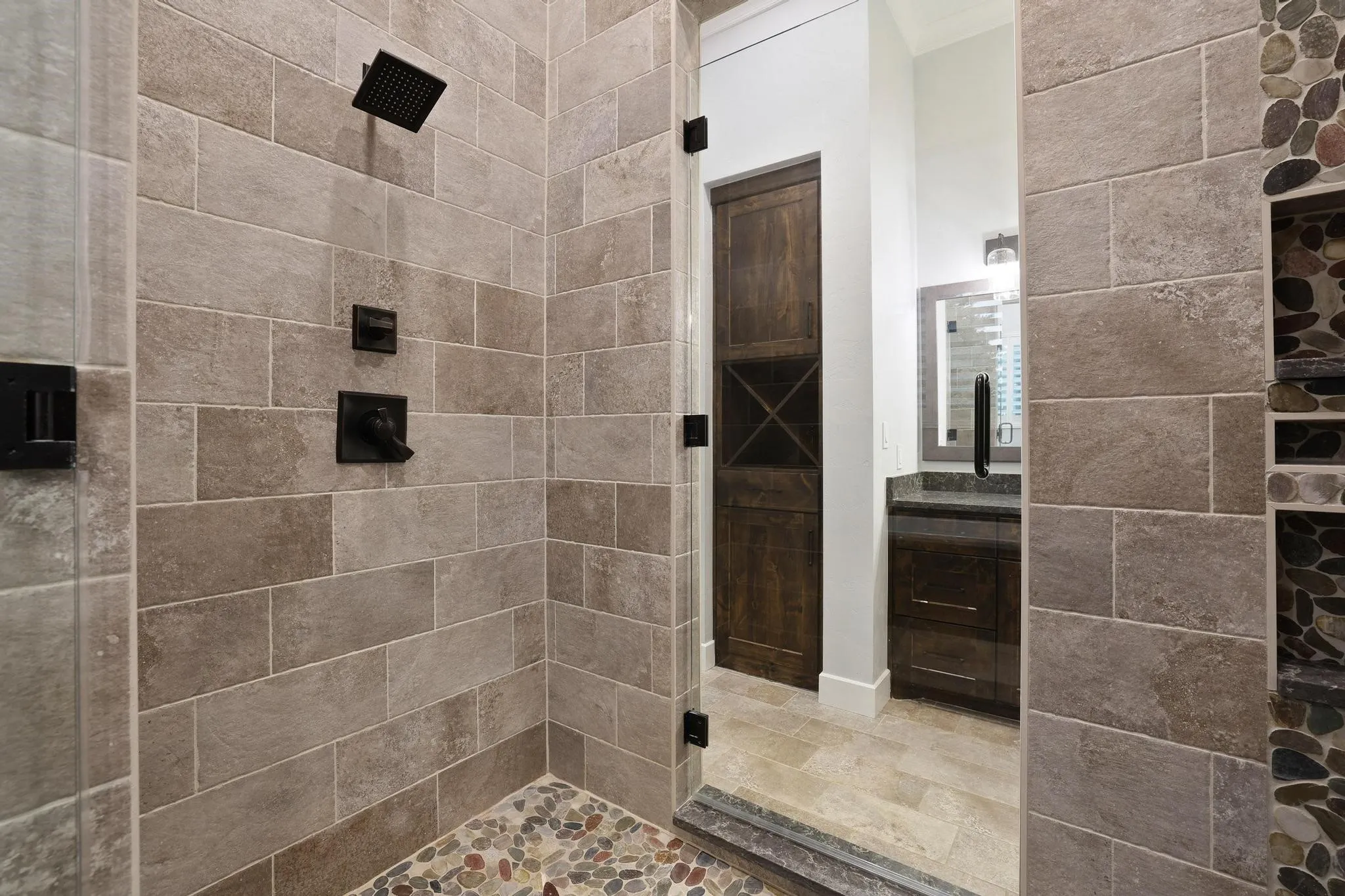 Walk-in shower featuring rectangular tile walls, a pebble-stone floor, and matte black fixtures including a rainfall shower head