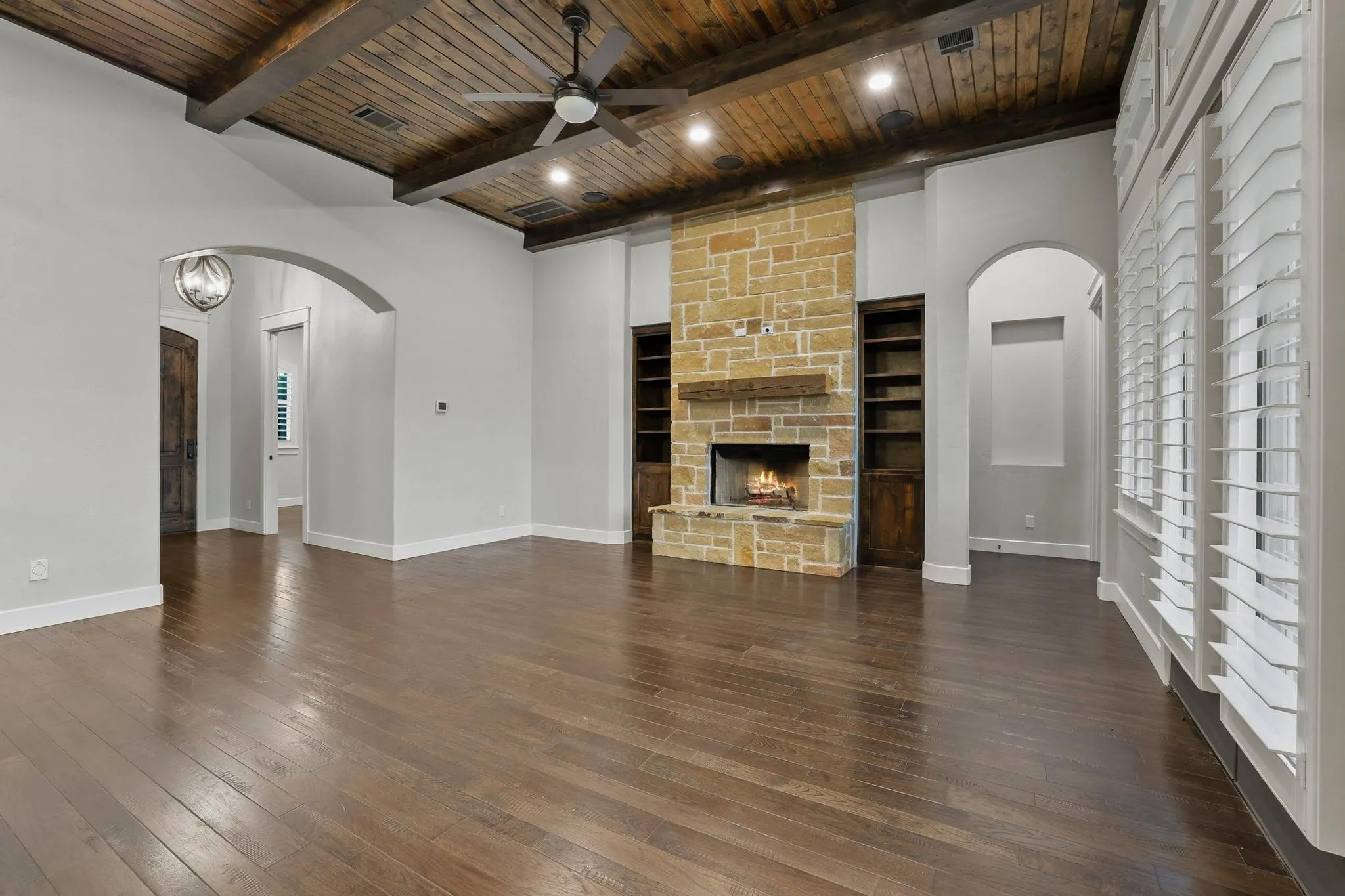 Spacious living area featuring wood-finish flooring, a stone fireplace with a wood mantel, and built-in shelving