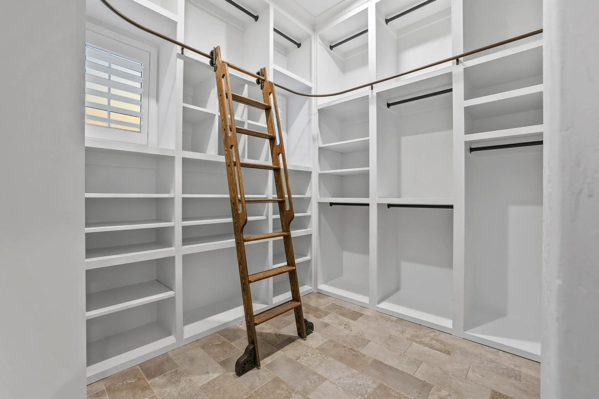Walk-in closet featuring extensive built-in shelving, multiple hanging rods, and a rolling ladder for access