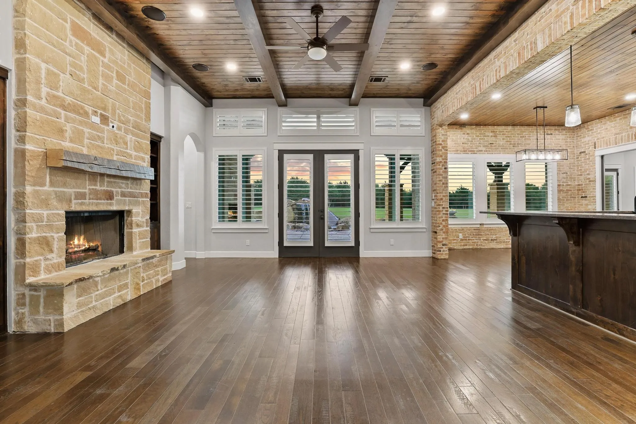 Spacious living area featuring wood-finish flooring, a stone-clad fireplace with a hearth and mantel, and a wood plank ceiling with exposed beams