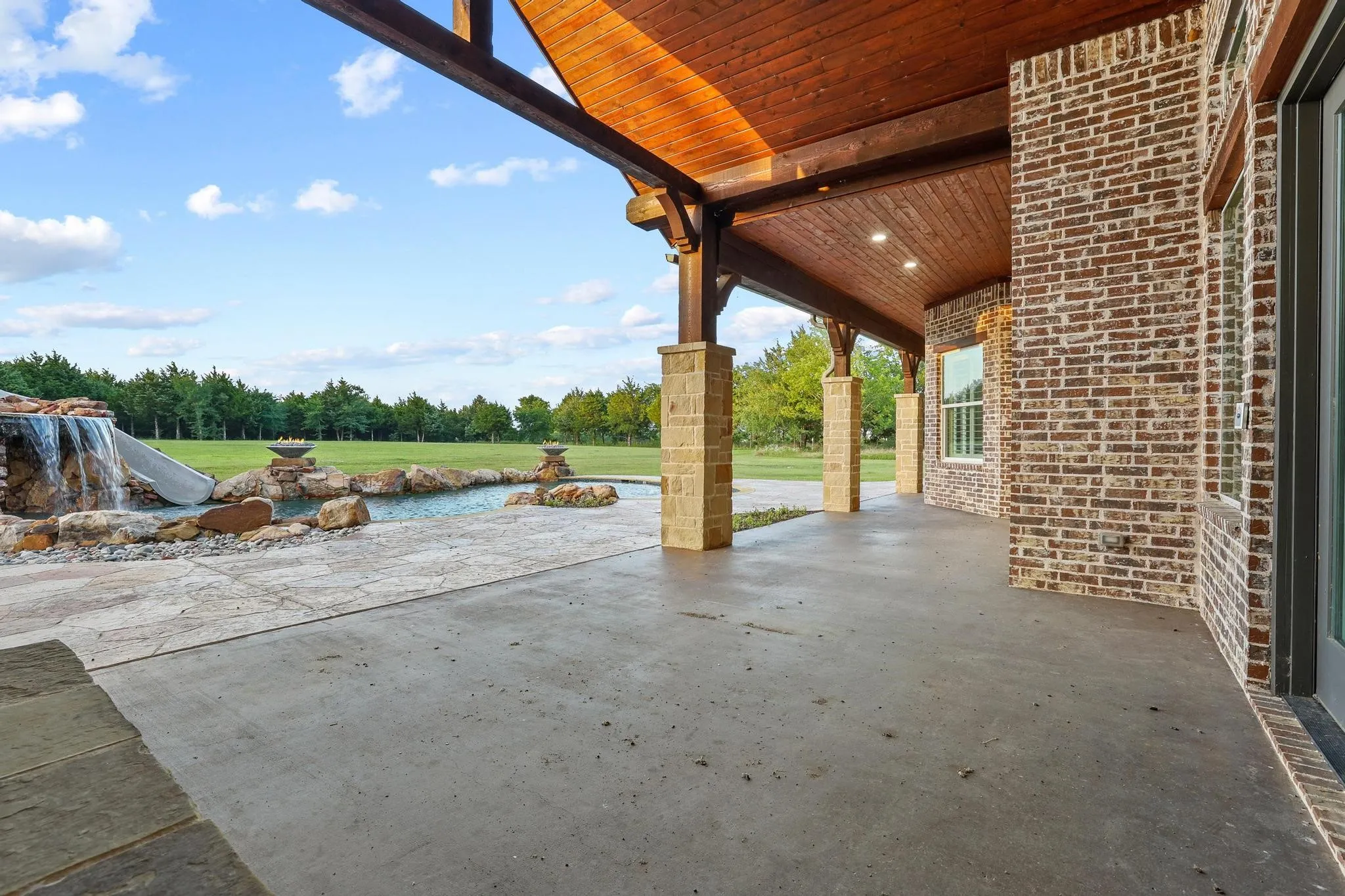 Expansive covered patio featuring a rich wood-finish ceiling, recessed lighting, and stone-clad support columns