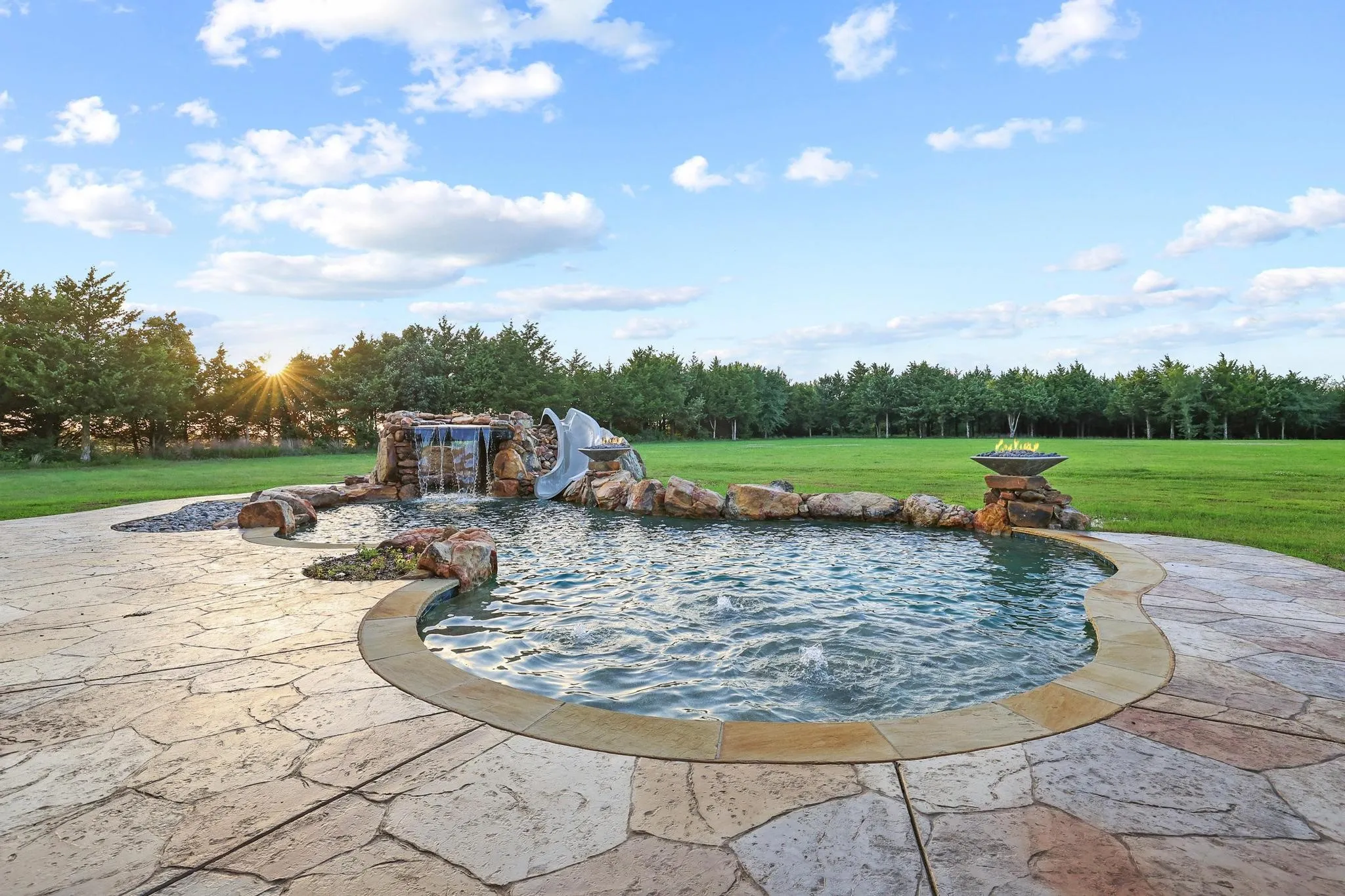Freeform swimming pool featuring a waterfall, rock features, a built-in slide, and a fire bowl